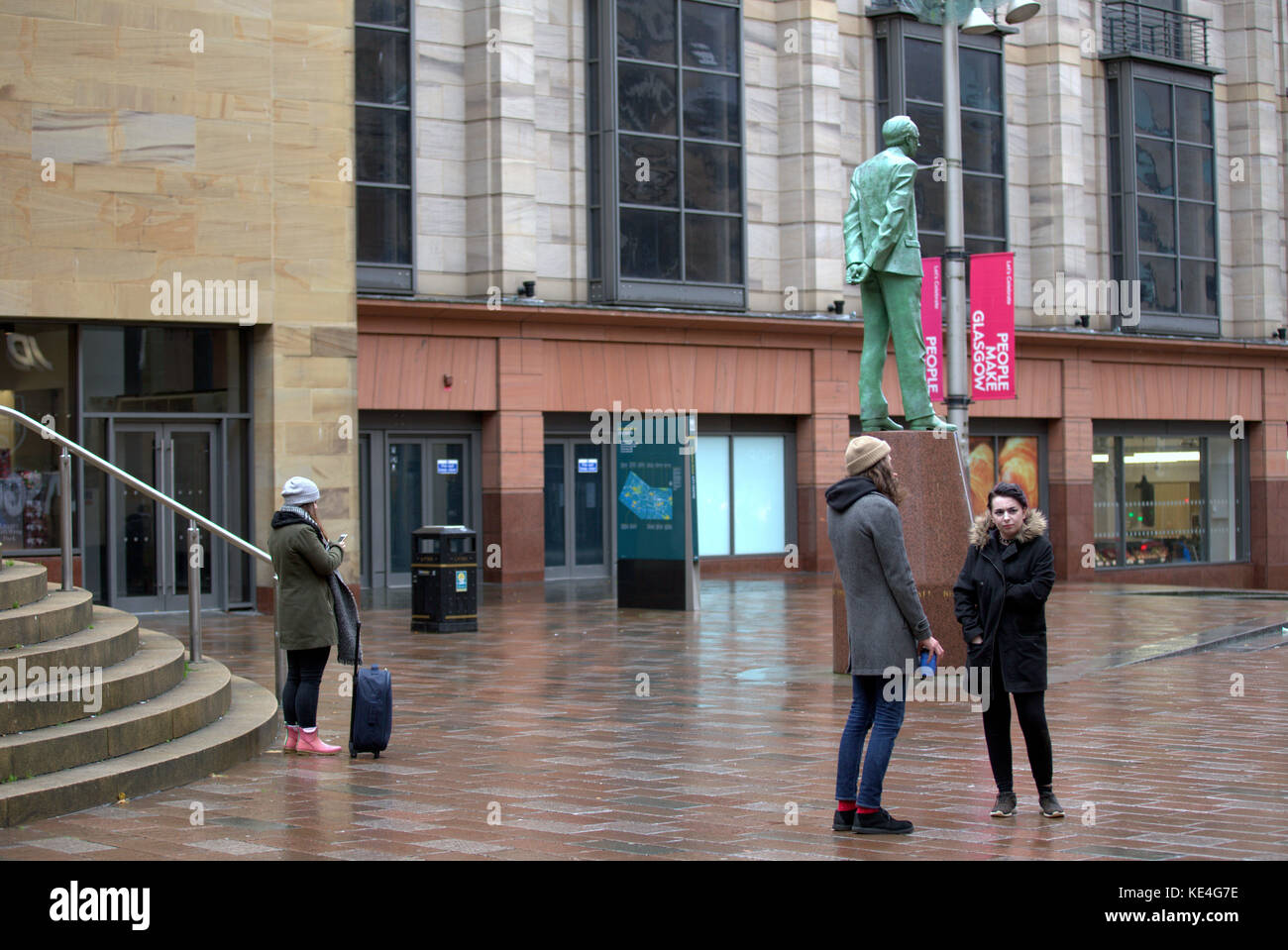 Galeries buchanan Rue Buchanan étapes à la statue donald Dewar jeunes attendant quelqu'un avec des rues humides Banque D'Images