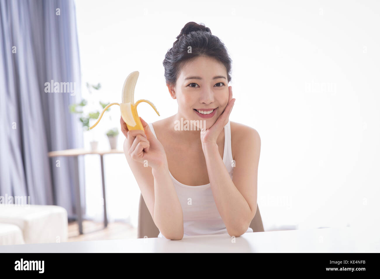 Portrait of young smiling woman eating banana slim Banque D'Images