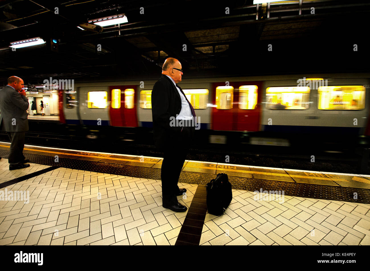 Londres, Angleterre, Royaume-Uni. Businessman en attente sur la plate-forme d'une station de métro de Londres Banque D'Images