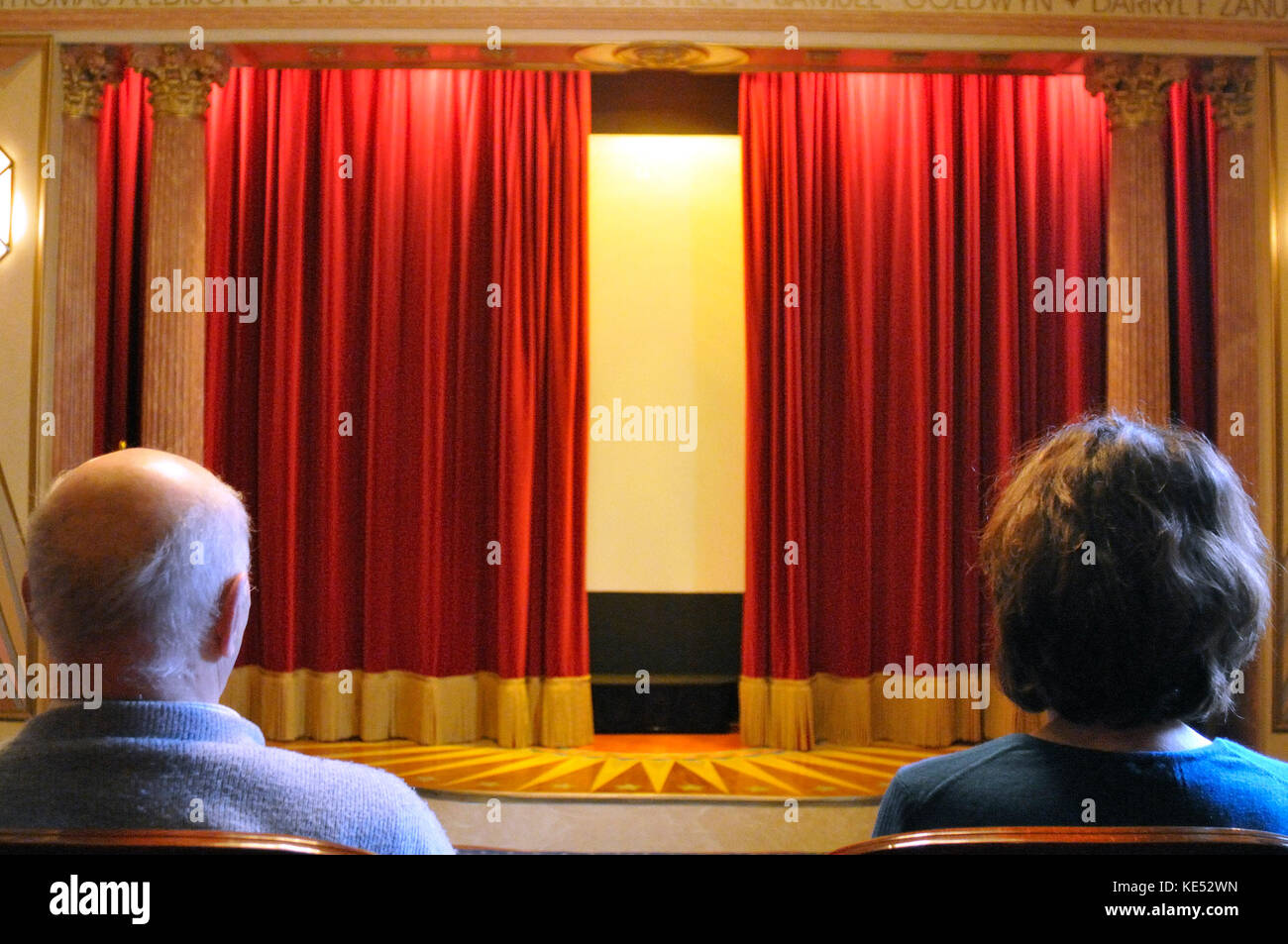 Des rideaux rouges de velours légèrement ouverte montre homme et femme regardant dans salle de cinéma construit en 1920, début des années 1930 style. Bien éclairée. Banque D'Images