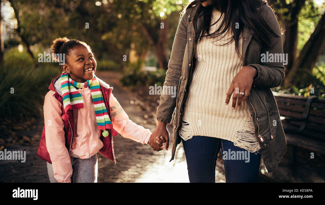 Cute little happy girl holding mains d'une femme et la marche à l'extérieur. Mère et fille se promener dehors et sourit. Banque D'Images