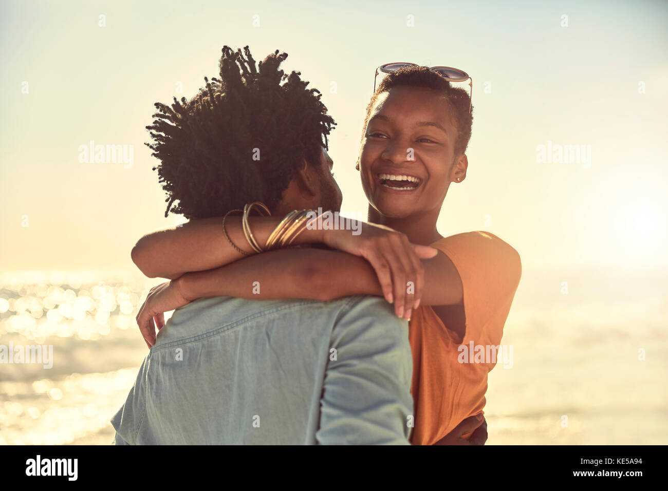 Un jeune couple en train de rire se embrassant sur une plage ensoleillée d'été Banque D'Images