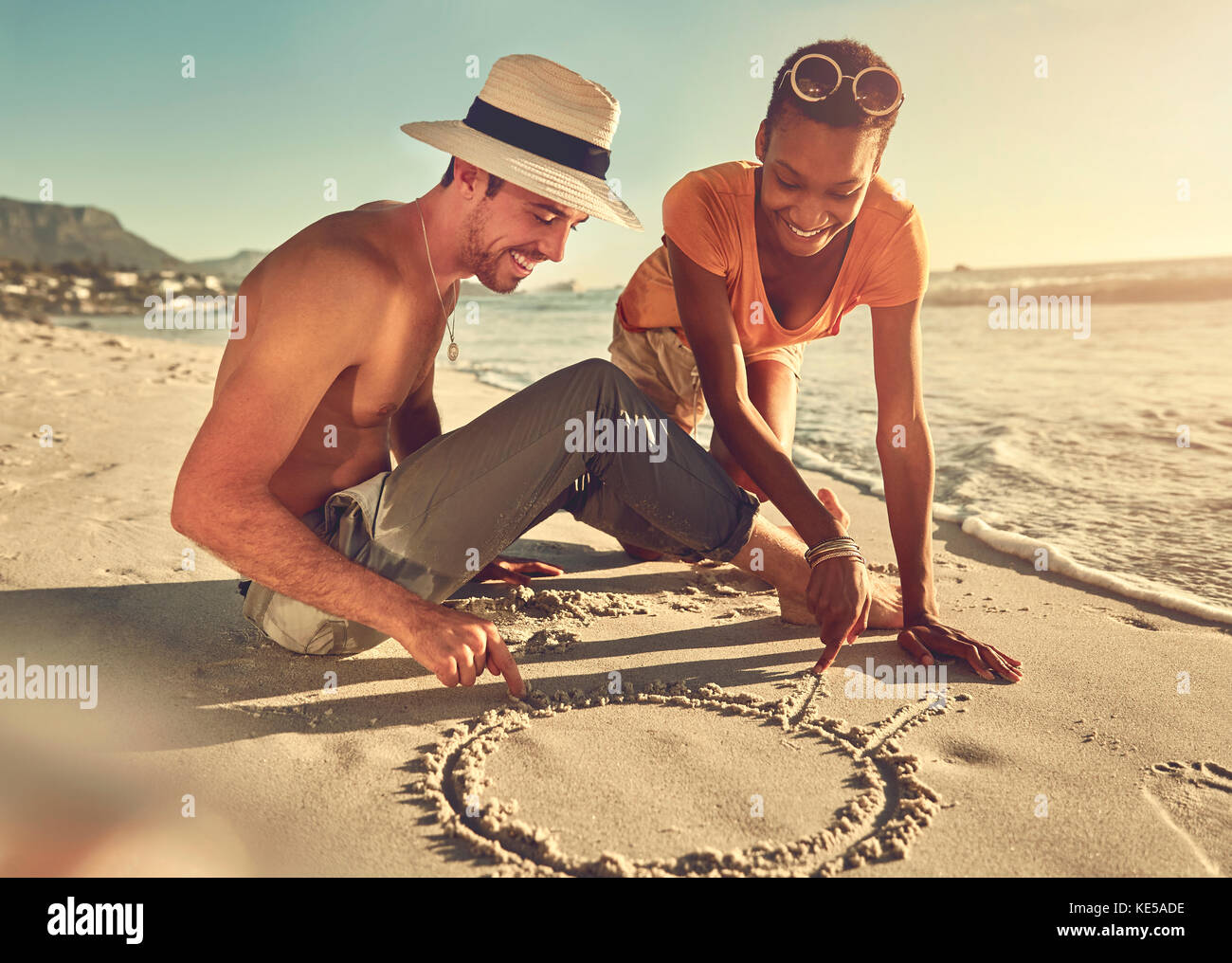 Jeune couple tirant dans le sable sur la plage ensoleillée d'été de l'océan Banque D'Images