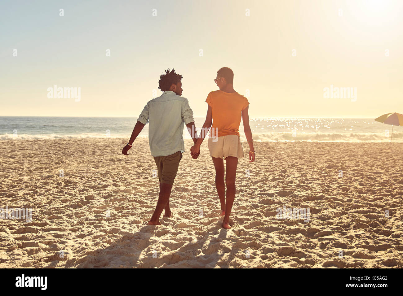 Jeune couple tenant les mains, marchant sur la plage ensoleillée d'été Banque D'Images