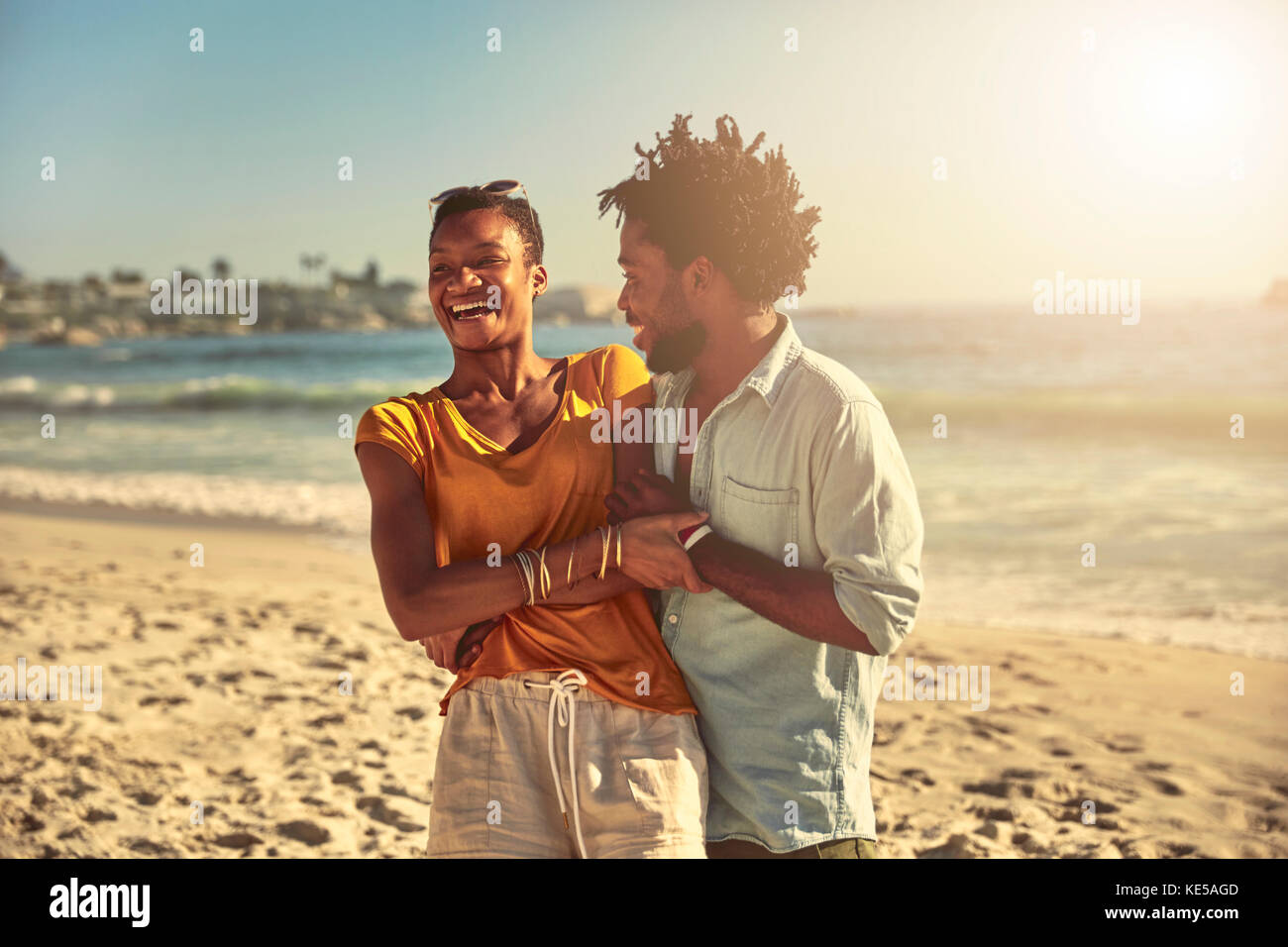 Un jeune couple enjoué qui se serre et rit sur l'océan ensoleillé d'été plage Banque D'Images