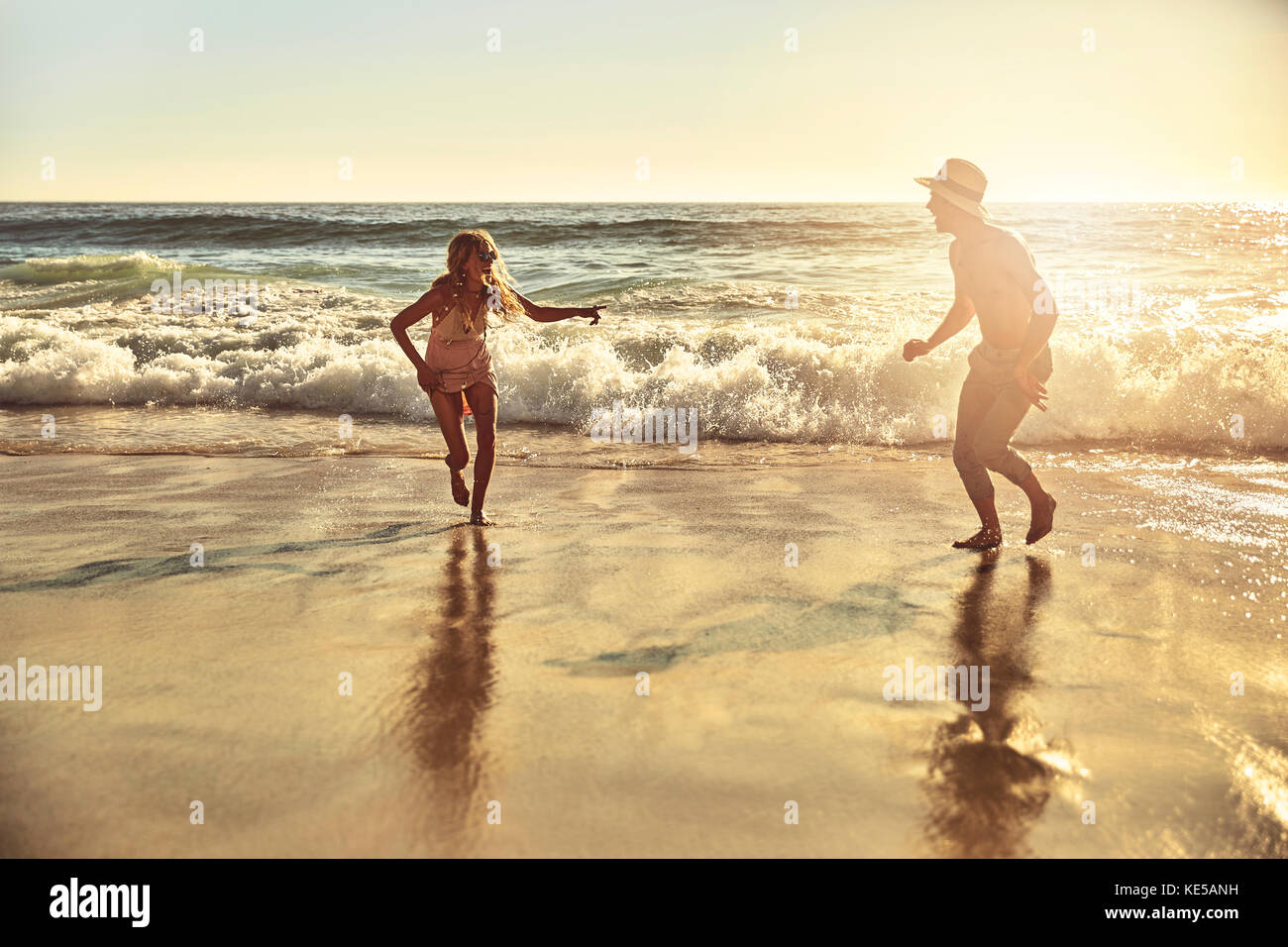 Jeune couple joueur qui court dans le sable humide l'été ensoleillé plage de l'océan Banque D'Images