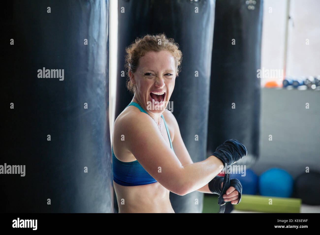 Portrait exubérant boxeur féminin hurlant, enveloppant les poignets dans la salle de gym Banque D'Images