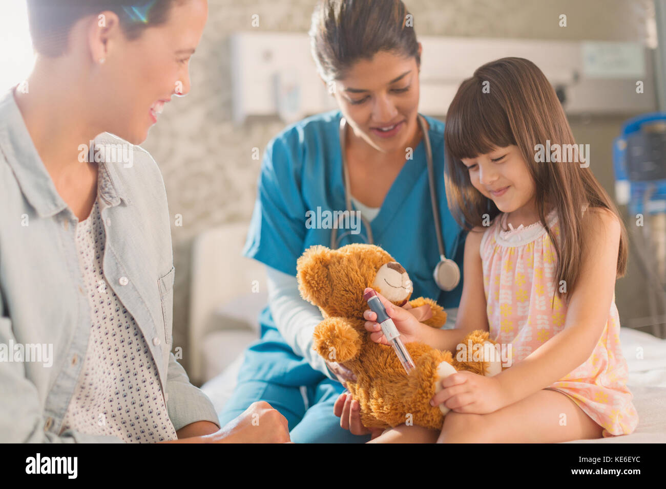 Une infirmière et une mère regardent une jeune patiente à l'aide d'un stylo à insuline sur l'ours en peluche Banque D'Images