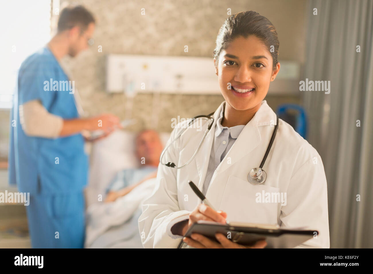 Portrait souriante femme médecin faisant des rondes, prenant des notes sur le bloc-notes du dossier médical dans la chambre d'hôpital Banque D'Images Portrait souriante femme médecin faisant des rondes, prenant des notes sur le bloc-notes du dossier médical dans la chambre d'hôpital Banque D'Images