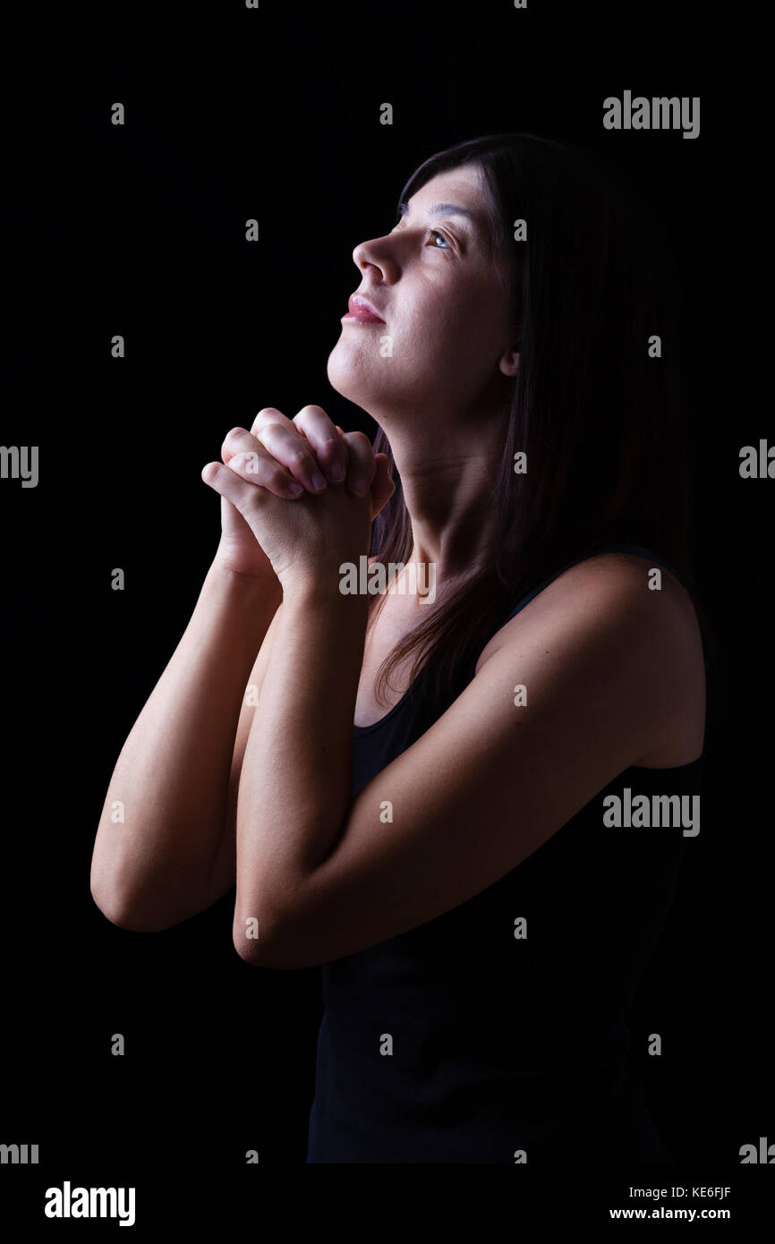 Femme en prière dans l'adoration fidèle à Dieu jusqu'à la dans l'espoir, avec les mains croisées et de ferveur religieuse sur un fond noir. foi prière sourire souriant Banque D'Images
