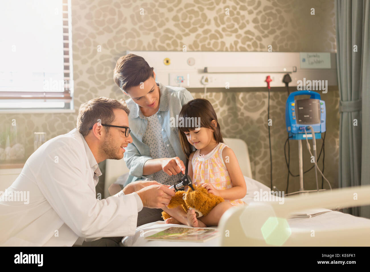 Médecin de sexe masculin utilisant un otoscope sur l'ours en peluche d'une jeune fille dans la chambre d'hôpital Banque D'Images