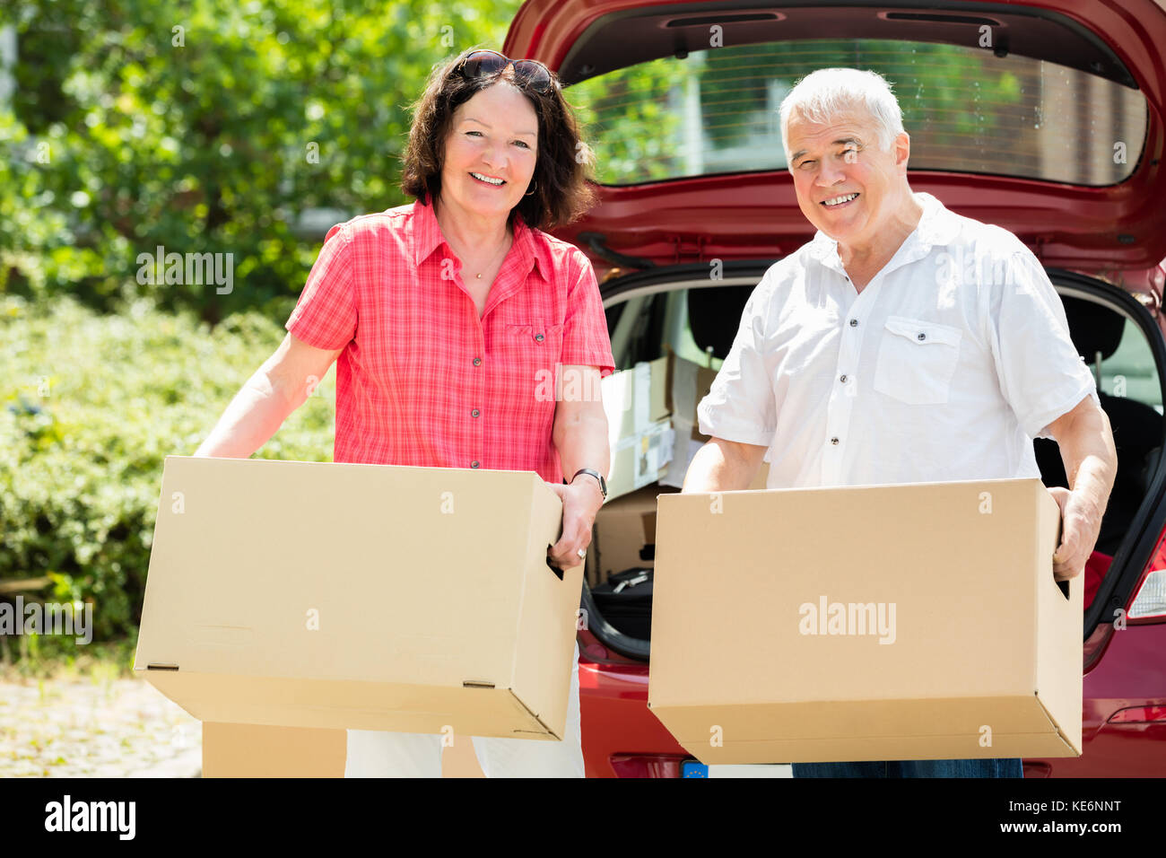 Happy Senior Couple standing in front of Car Holding Cardboard Box Banque D'Images