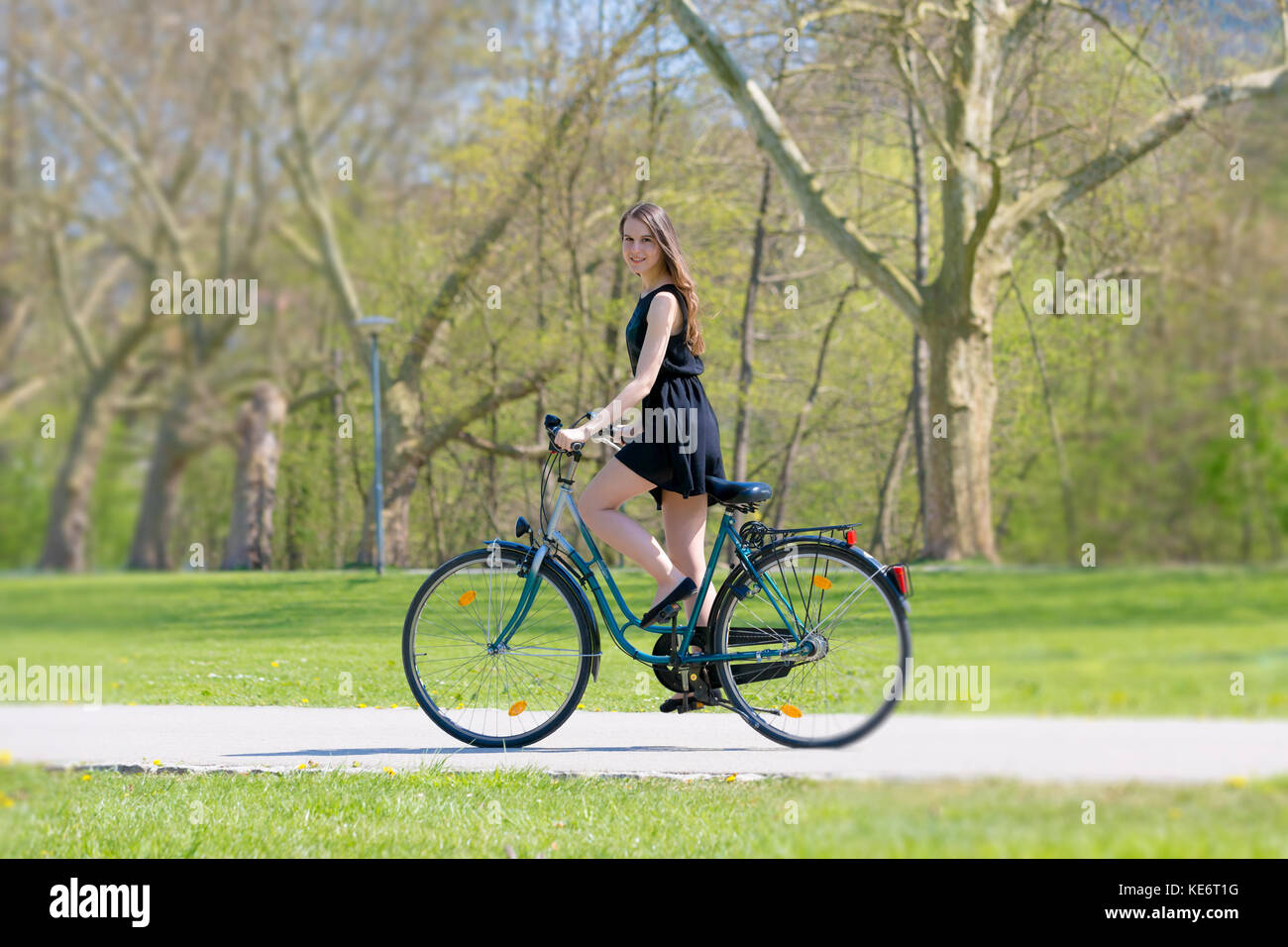 Vue portrait of girl sur location portant sur noir robe courte. Les jeunes femme heureuse équitation le long de la route sur vert printemps parc extérieur. Jeune fille sportive ri Banque D'Images