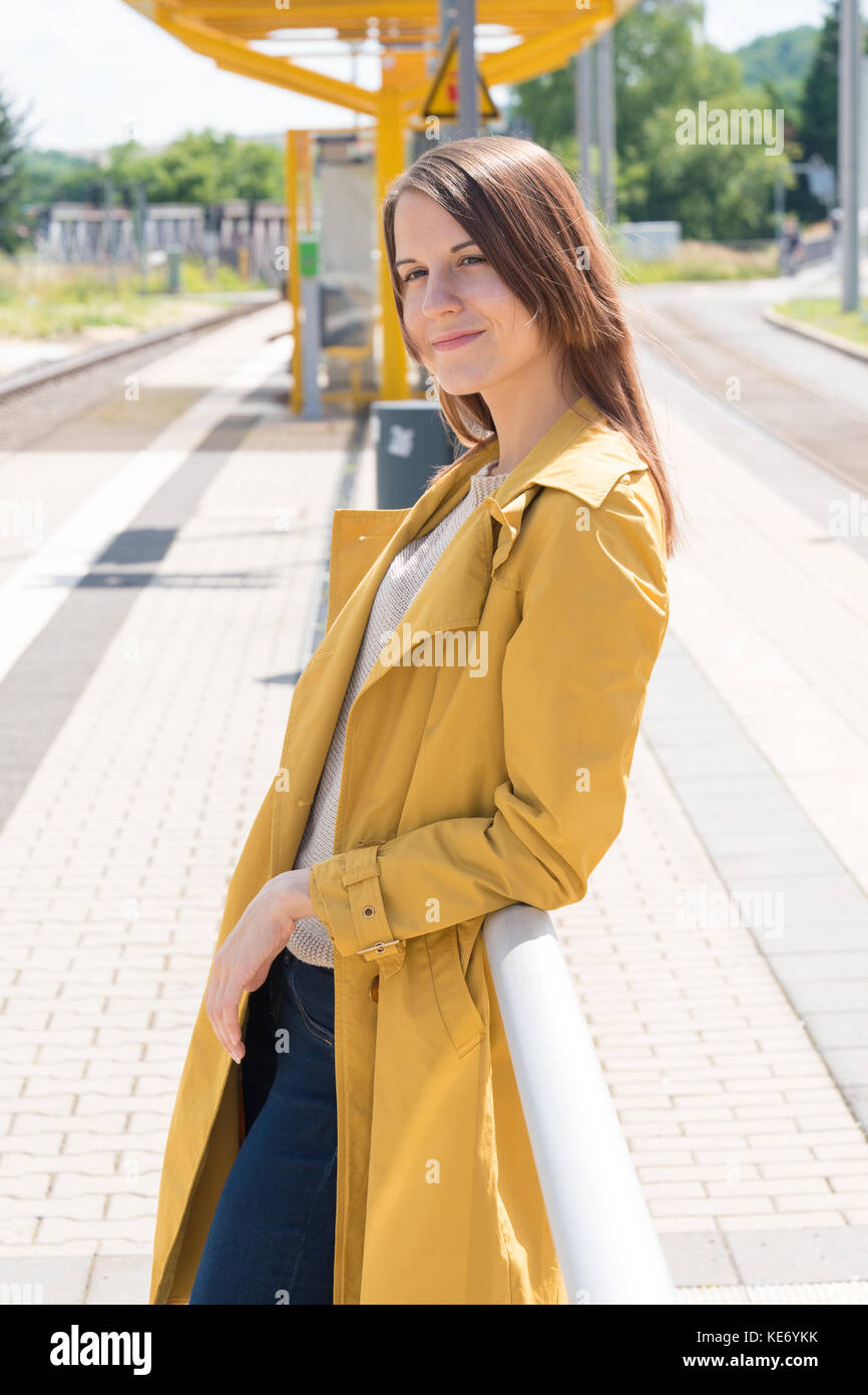 Jeune femme dans un ciré en attente d'un train en gare Banque D'Images