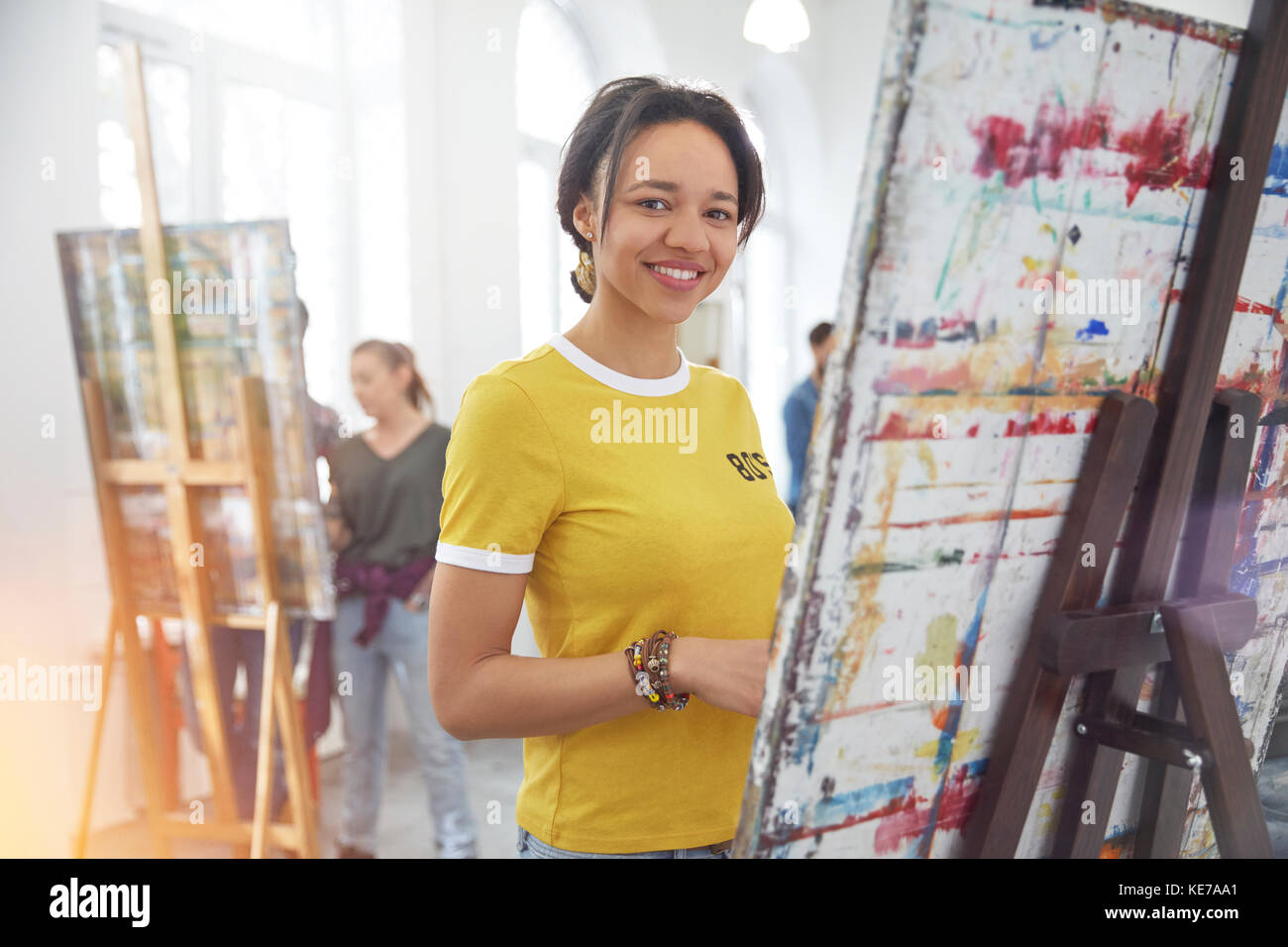 Portrait souriant artiste femme peinture à l'eseasel en classe d'art studio Banque D'Images
