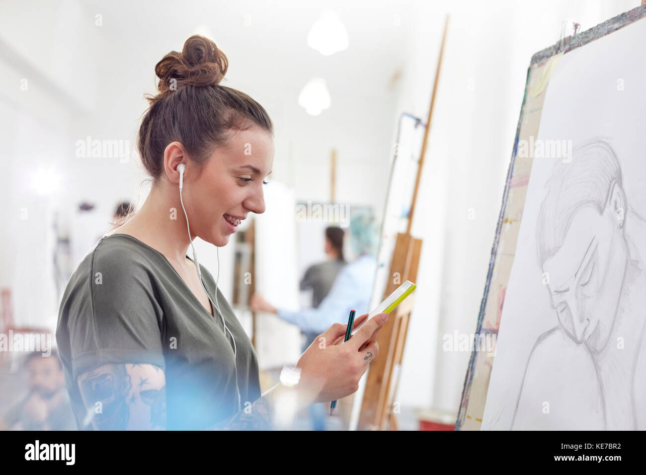 Artiste féminine souriante avec casque pour écouter de la musique et dessiner en studio de classe d'art Banque D'Images