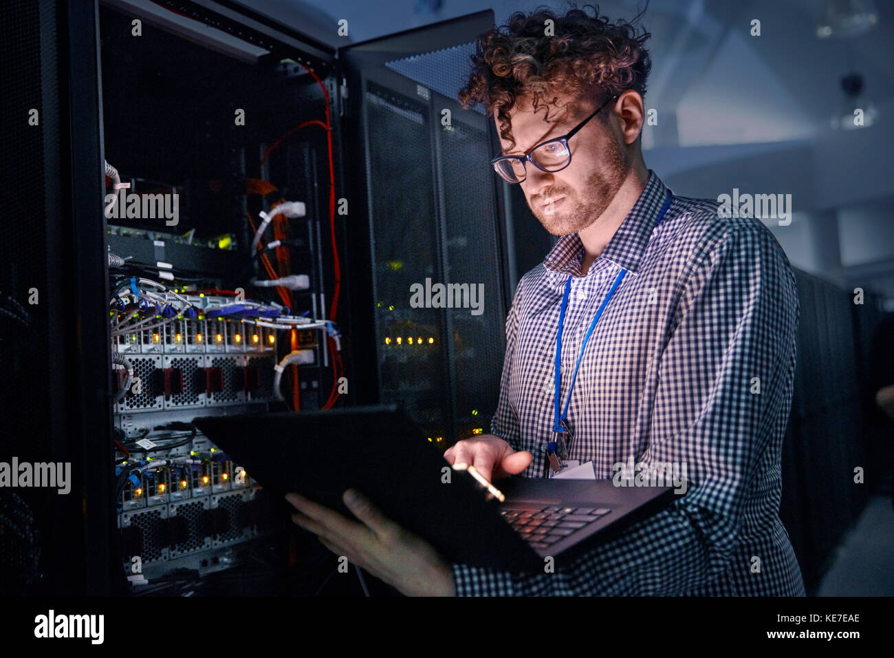 Technicien INFORMATIQUE spécialisé travaillant sur un ordinateur portable dans un serveur sombre chambre Banque D'Images