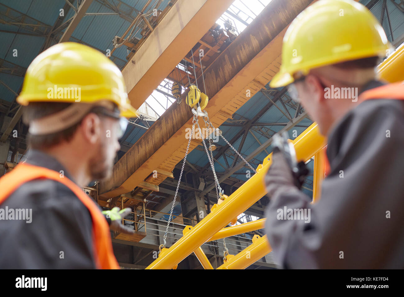 Travailleur masculin utilisant un talkie-walkie pour guider l'équipement d'abaissement de grue hydraulique en usine Banque D'Images
