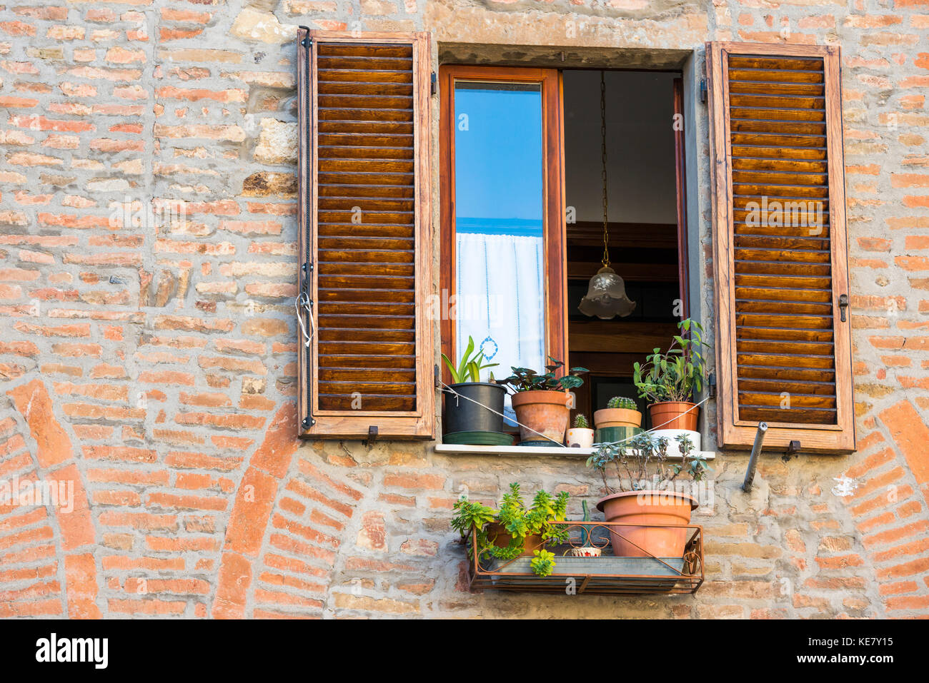 Fermer la vue d'une façade de maison en brique Montepulciano avec fenêtre ouverte, pots et stores grillagées, Toscane, Italie Banque D'Images