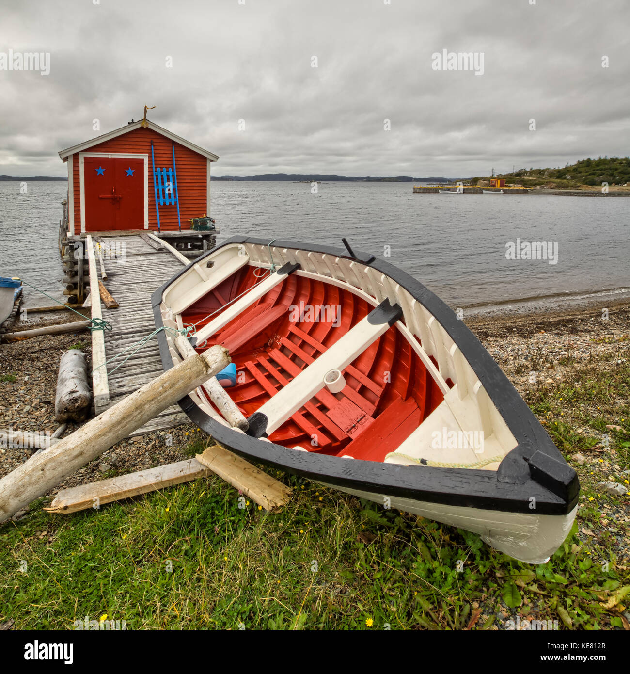 Un canoë rouge et blanc s'étend sur la rive avec un abri de pêche rouge le long du bord de l'eau de la côte Atlantique, Terre-Neuve, Canada Banque D'Images