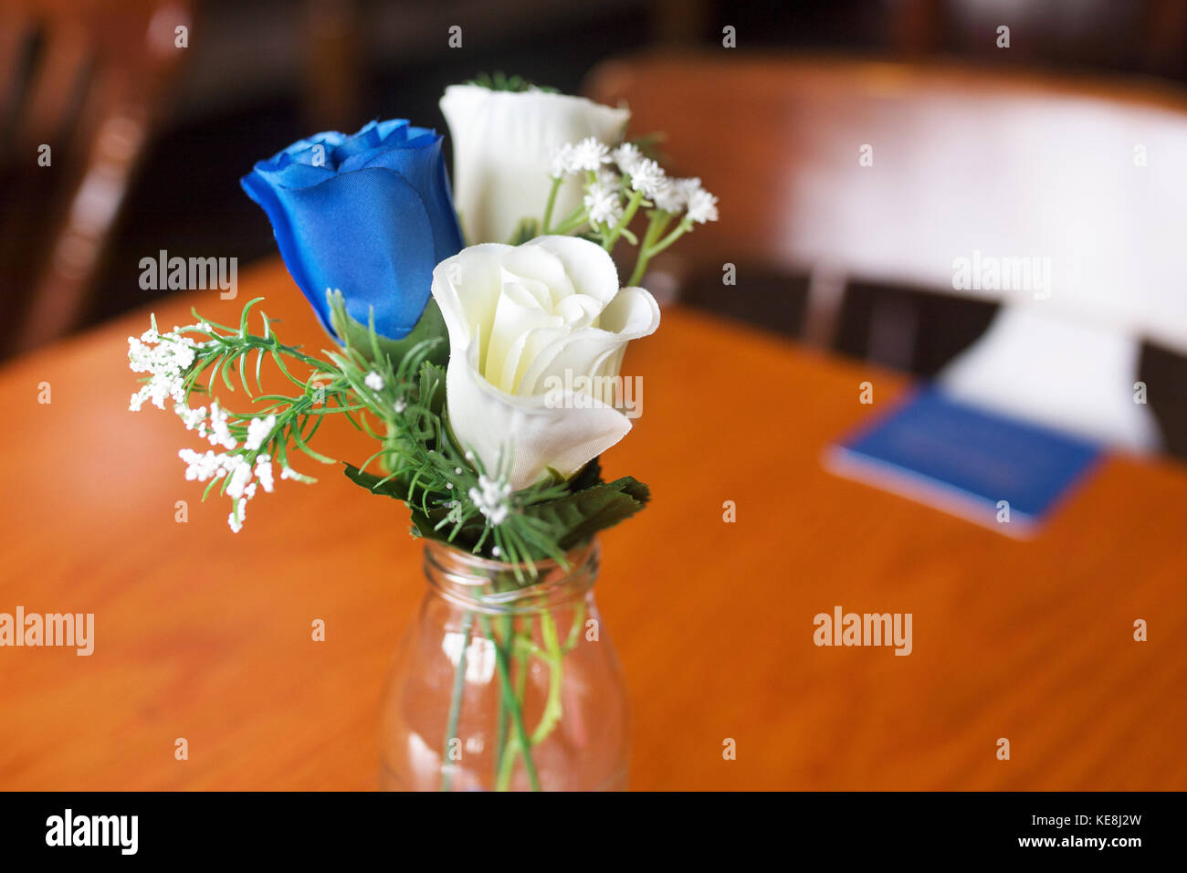 Close up d'atrificial roses bleu et blanc comme un décor de table dans un petit vase en verre à un mariage traditionnel anglais au Royaume-Uni Banque D'Images