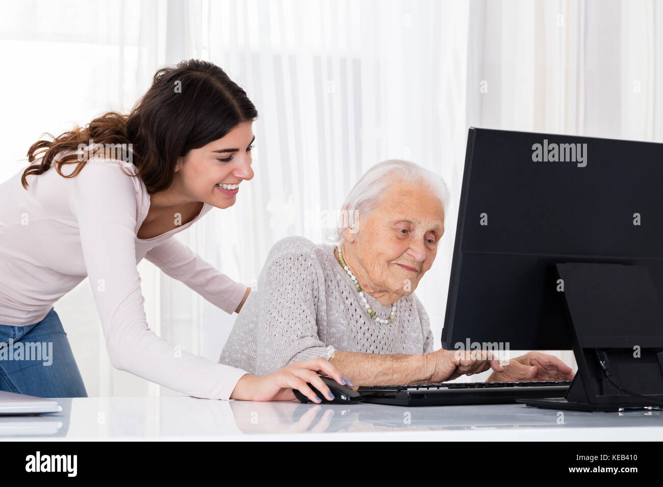 Jeune femme d'aider sa grand-mère pour l'aide d'un ordinateur portable sur un bureau à la maison Banque D'Images