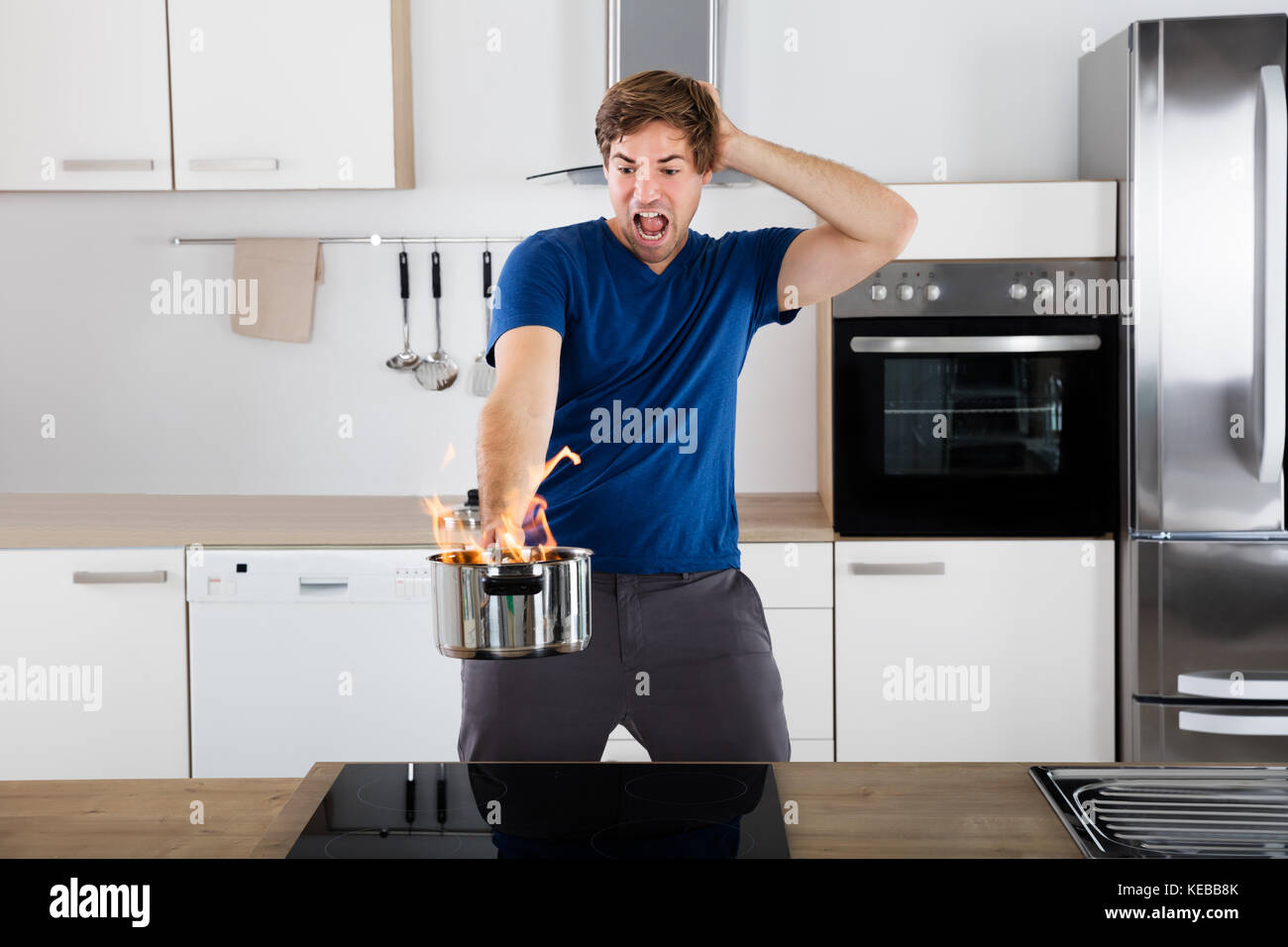 Young Man Holding surpris en feu dans l'ustensile Cuisine Banque D'Images