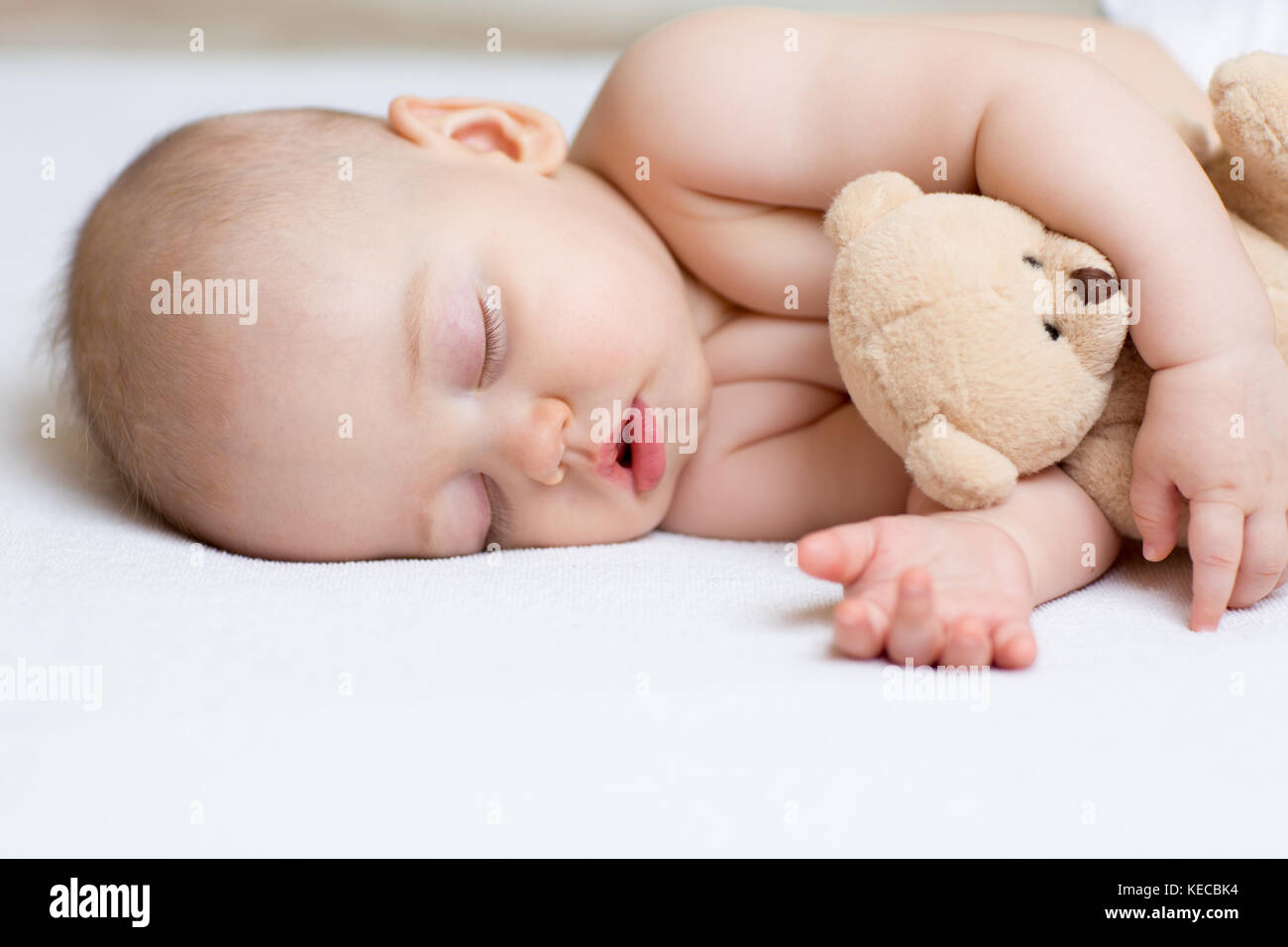 Nouveau-né bébé à dormir dans le lit, tenant un ours en peluche. Banque D'Images