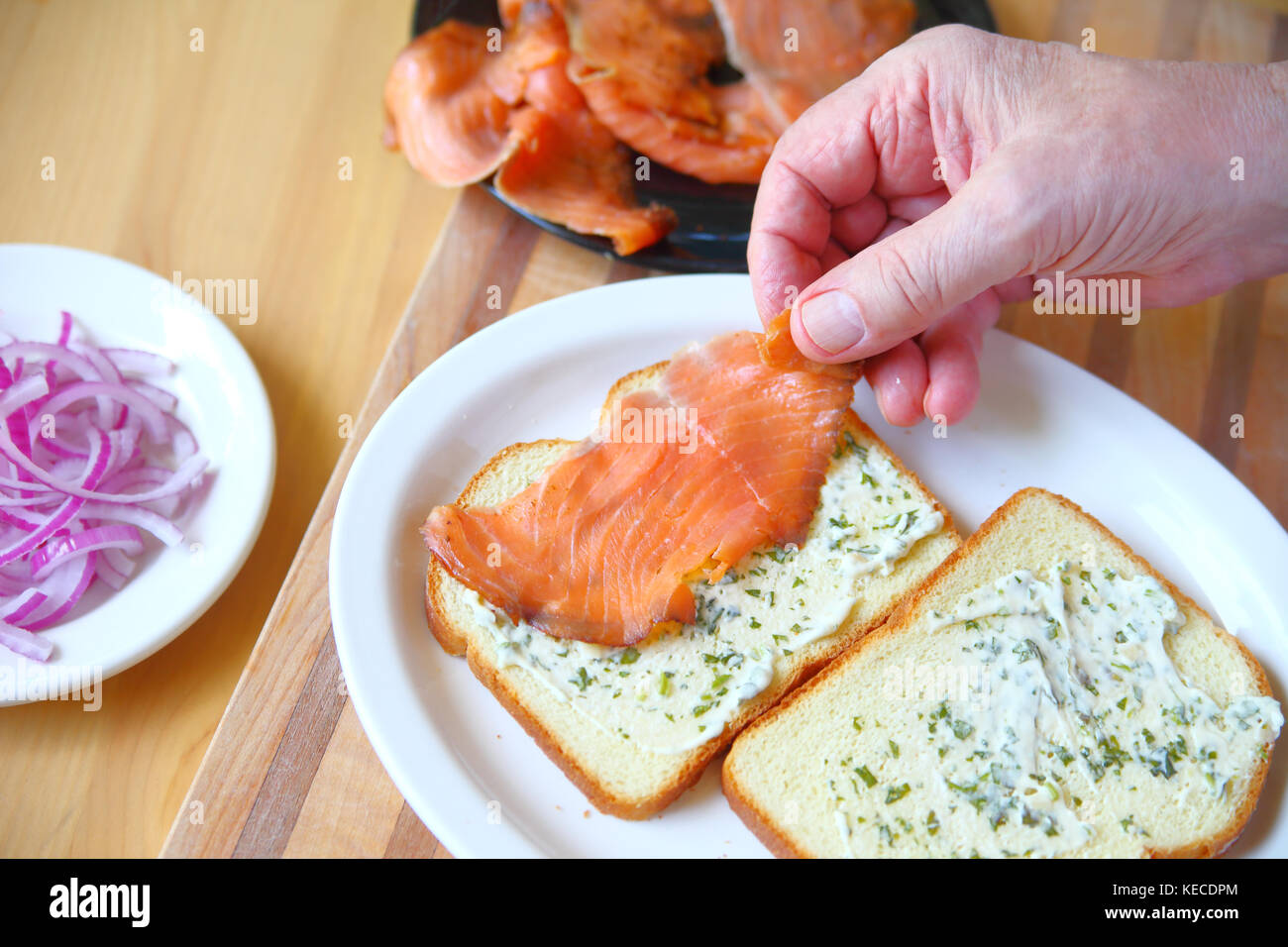 Un homme met sur pied un sandwich de saumon fumé et l'oignon sur le pain avec la mayonnaise aux fines herbes Banque D'Images