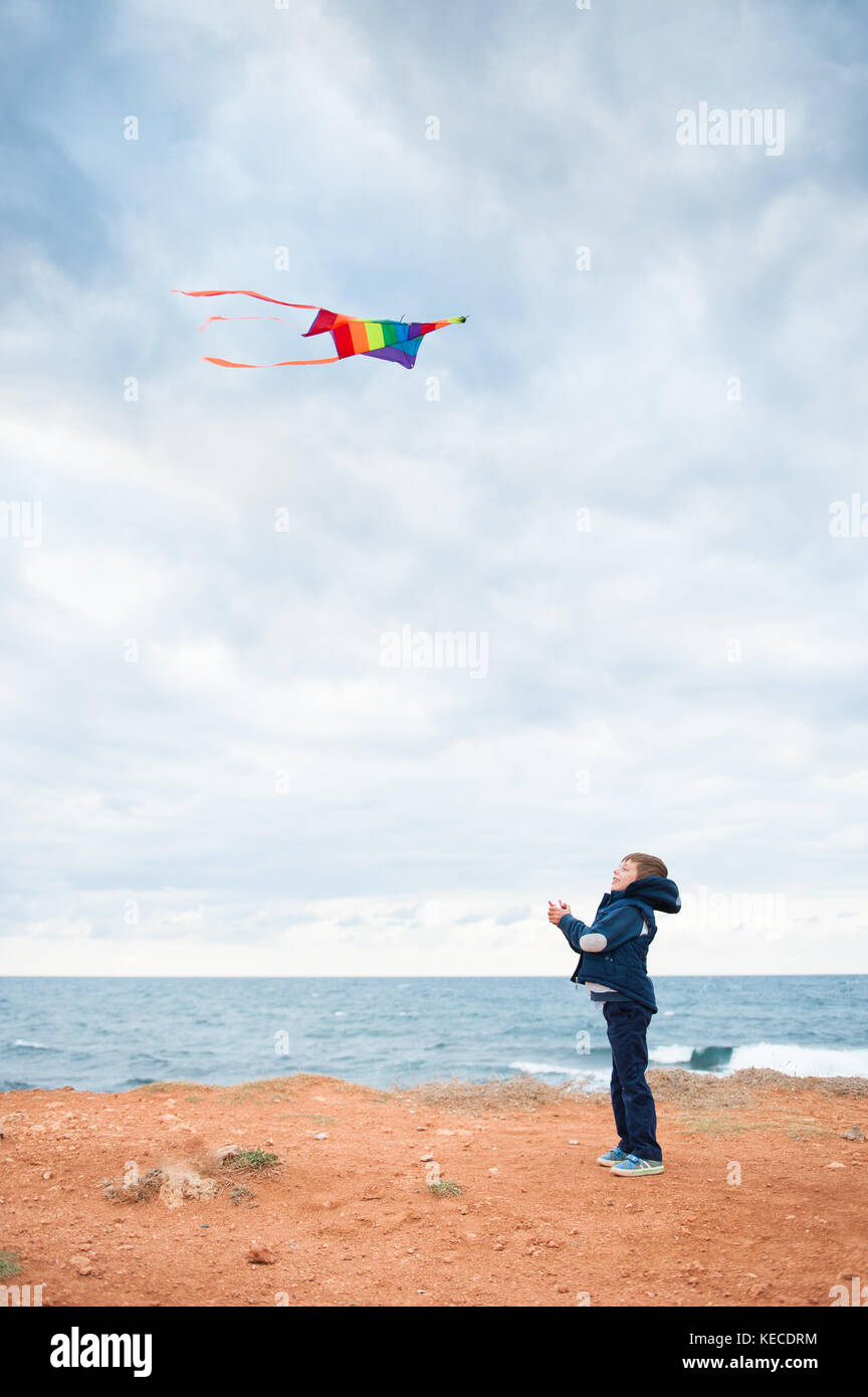 Young boy petit mignon portant veste automne jouer flying kite debout sur la rive près de mer agitée Banque D'Images