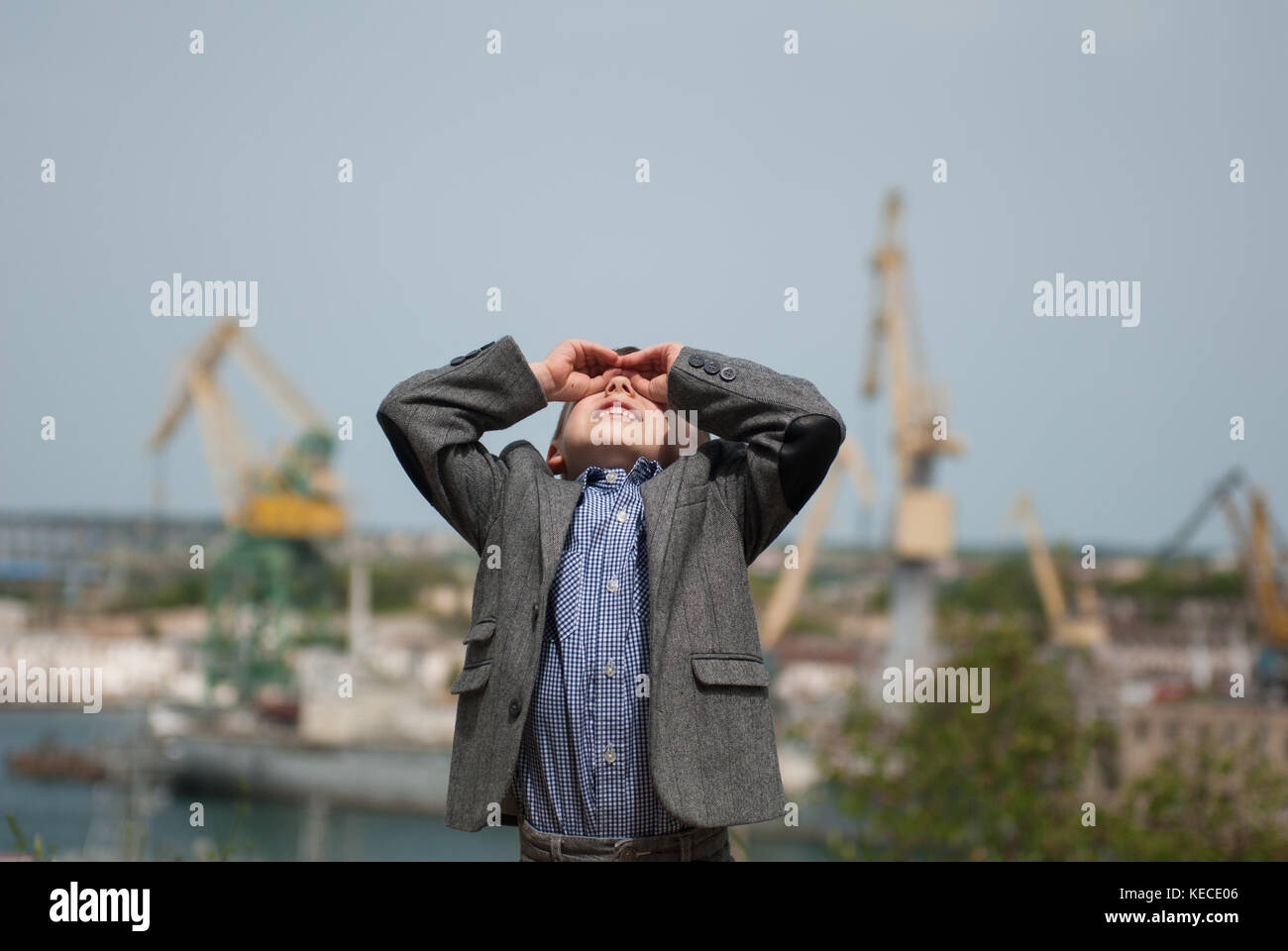 Smiling little boy wearing jacket à la recherche jusqu'à l'aide de ses mains dans la forme de jumelles Banque D'Images