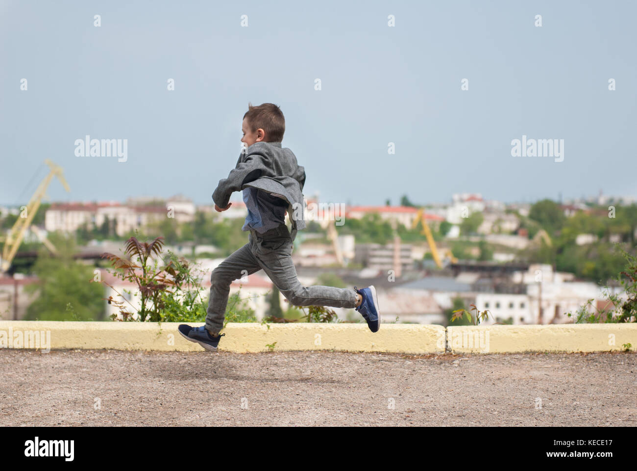 Petit garçon en bonne santé dans une veste en marche le long de l'asphalte le long du paysage urbain historique Banque D'Images