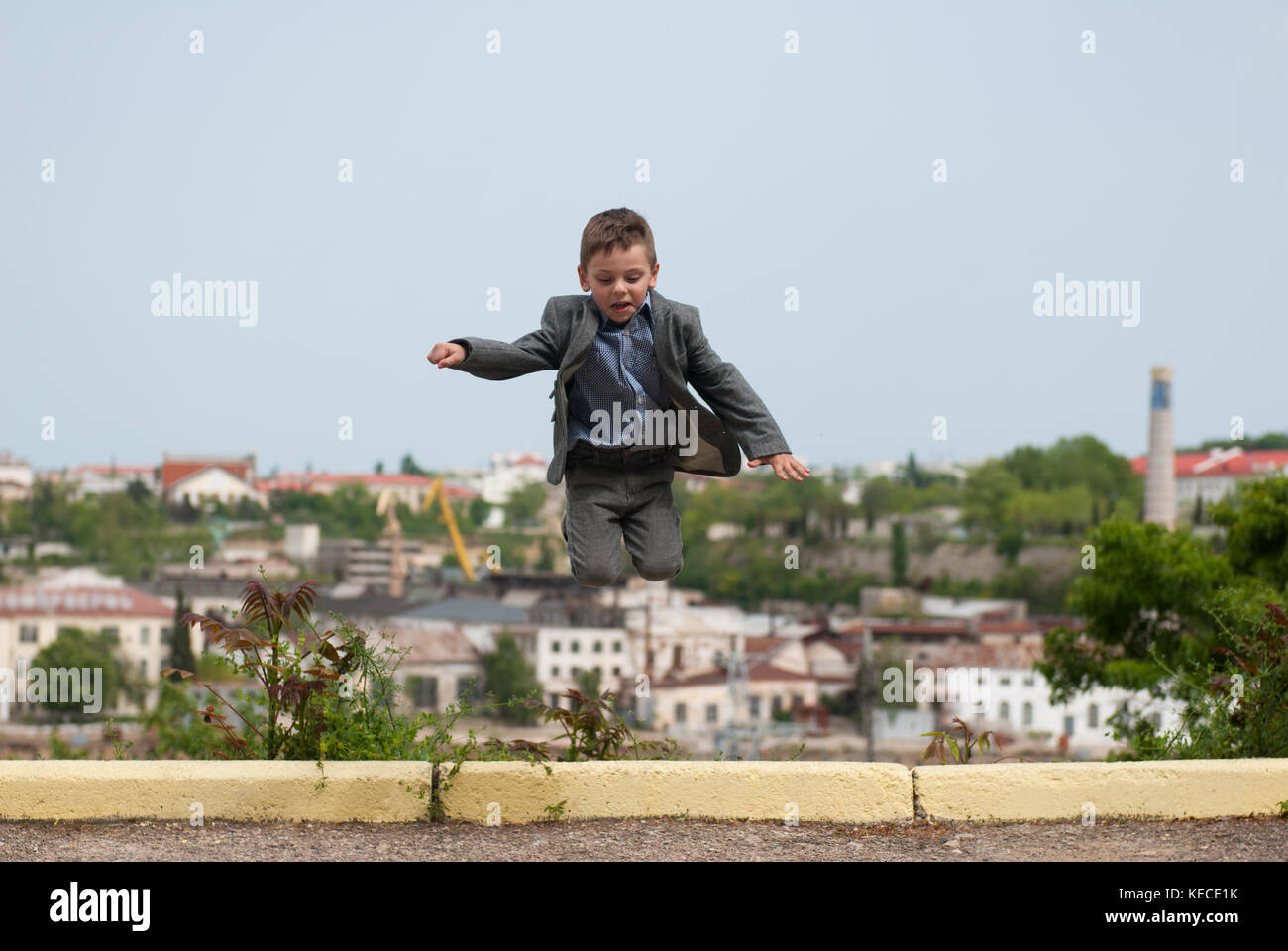 Petit garçon portant un costume sautant sur l'arrière-plan de la ville Banque D'Images