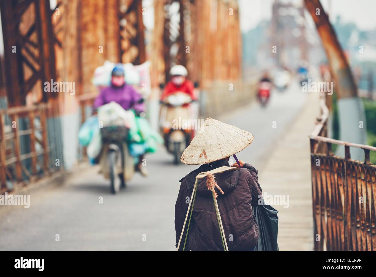 Vendeur de rue vietnamiens mène beaucoup de choses à travers le pont long bien à Hanoï, au Vietnam. selective focus sur la coiffe traditionnelle. Banque D'Images