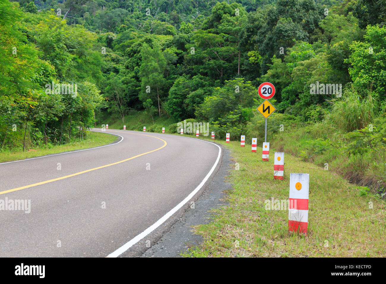 Route calme au pied d'une montagne avec des arbres verts et des panneaux de circulation. Banque D'Images