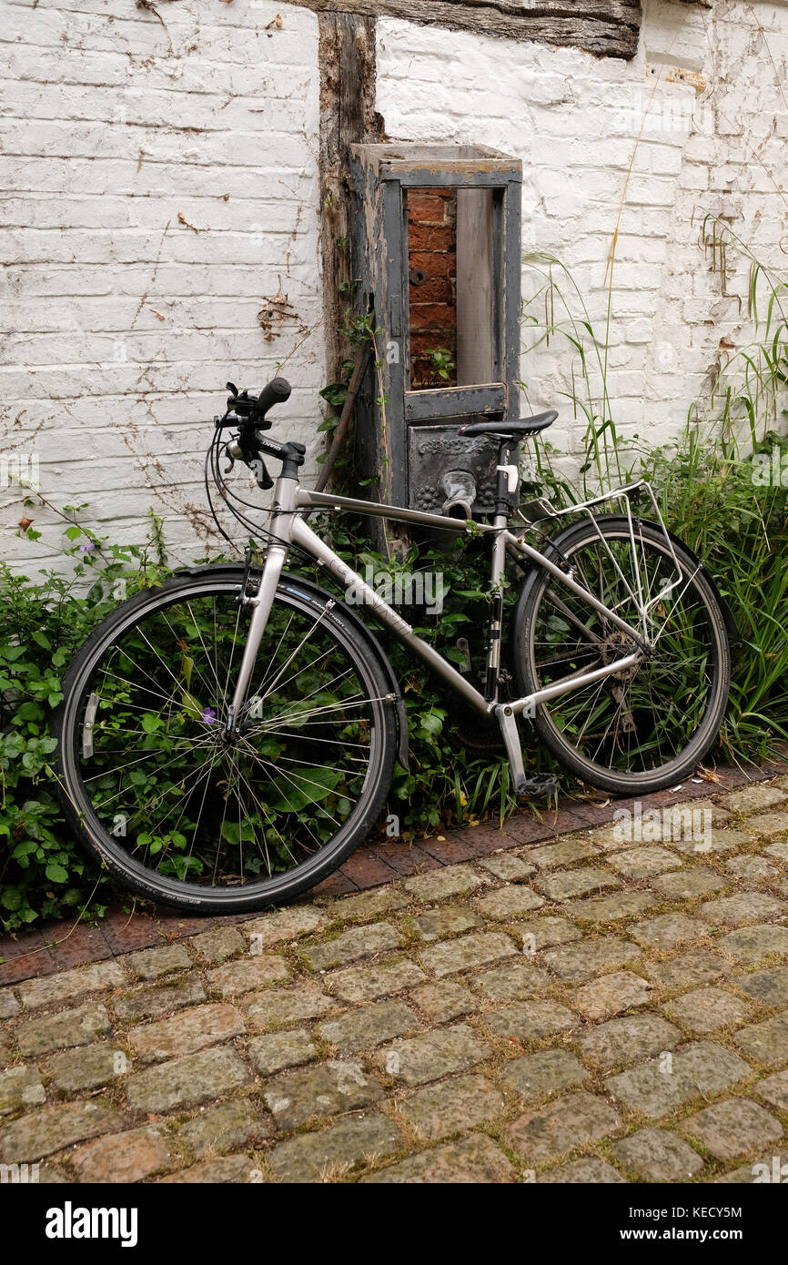 Juin 2017 - Location de vélo moderne à gauche appuyée contre un vieux mur in Thame, Oxfordshire, Angleterre. Banque D'Images