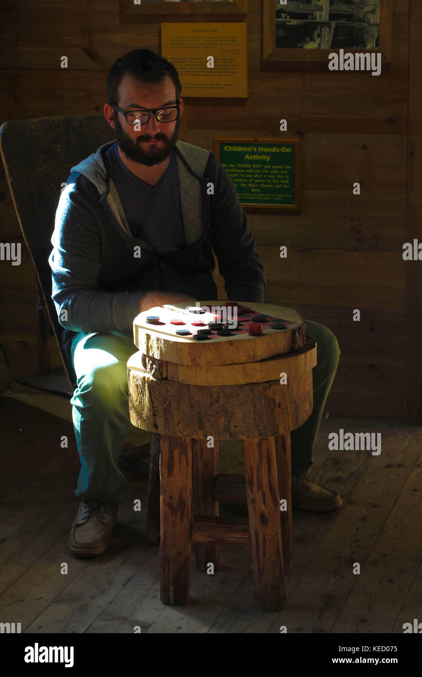 Un homme est assis à l'intérieur d'une cabane en rondins profitant d'un jeu de société appelé Checkers qui est à la mode ancienne Banque D'Images