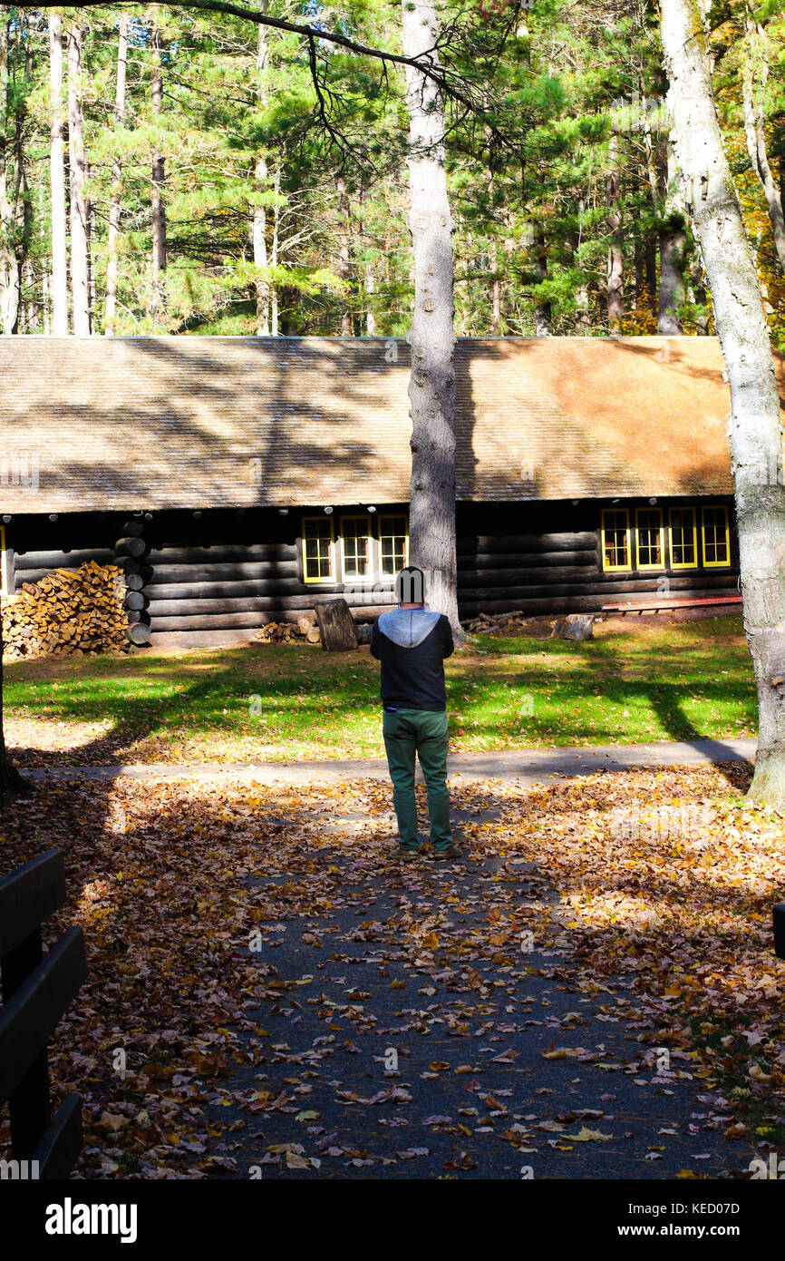 Un homme avec une cabine à l'arrière-plan bénéficie d'une belle journée d'automne dans le nord du Michigan entouré par les couleurs de l'automne dans les bois et parcs naturels Banque D'Images