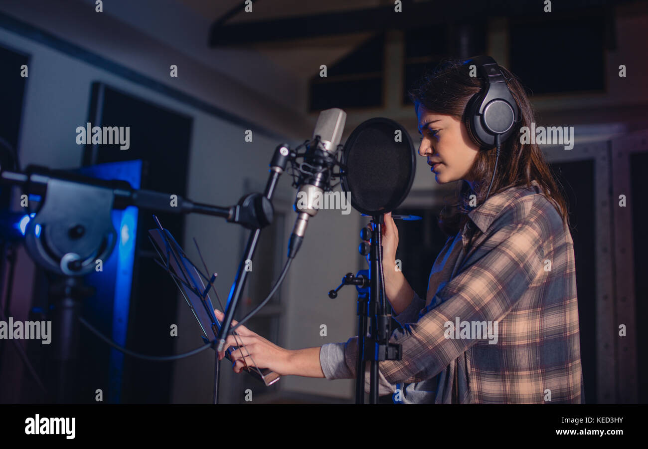 Femme enregistrer de la musique au un studio d'enregistrement professionnel. Chanteuse avec des écouteurs lecture lyrics. Banque D'Images