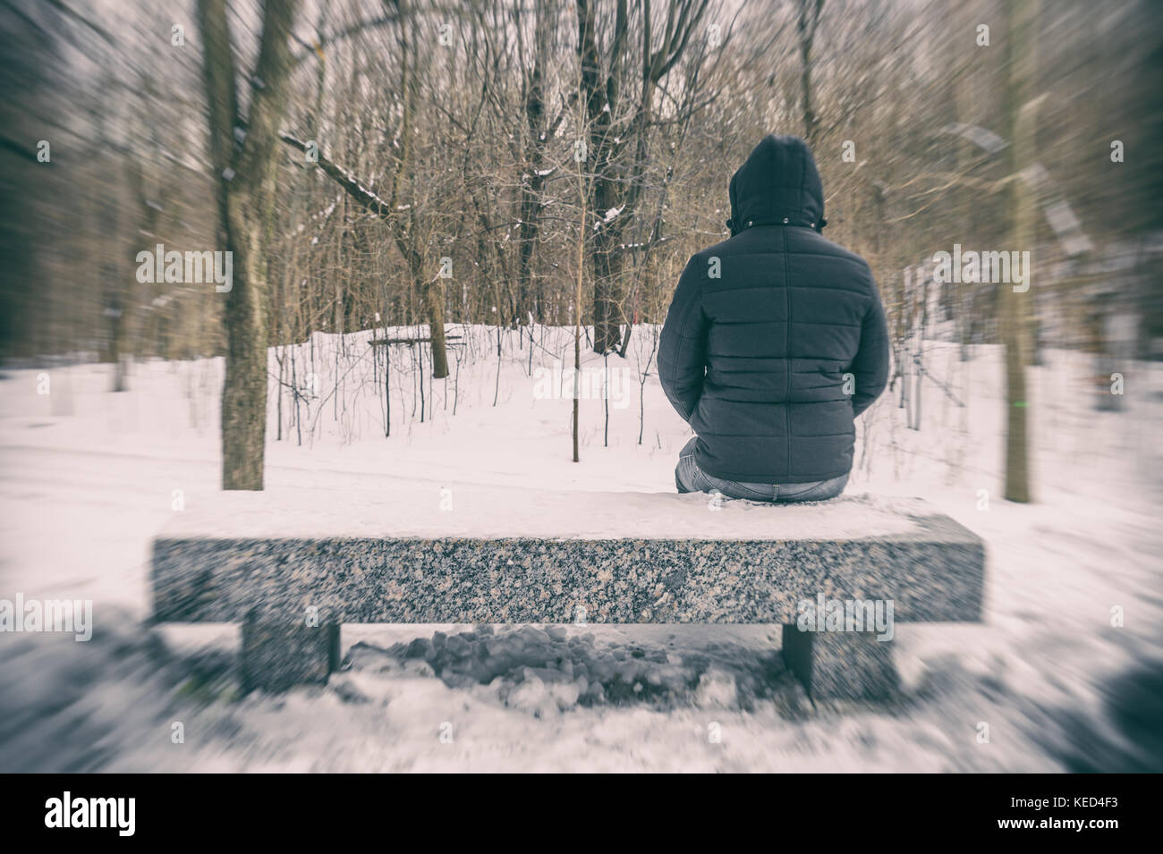 Homme assis sur un banc dans une forêt en hiver avec de la neige au sol Banque D'Images