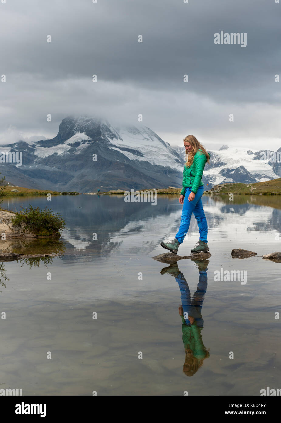 Randonneur marche sur des pierres dans l'eau, stellisee, couvertes de nuages Matterhorn, Valais, Suisse Banque D'Images