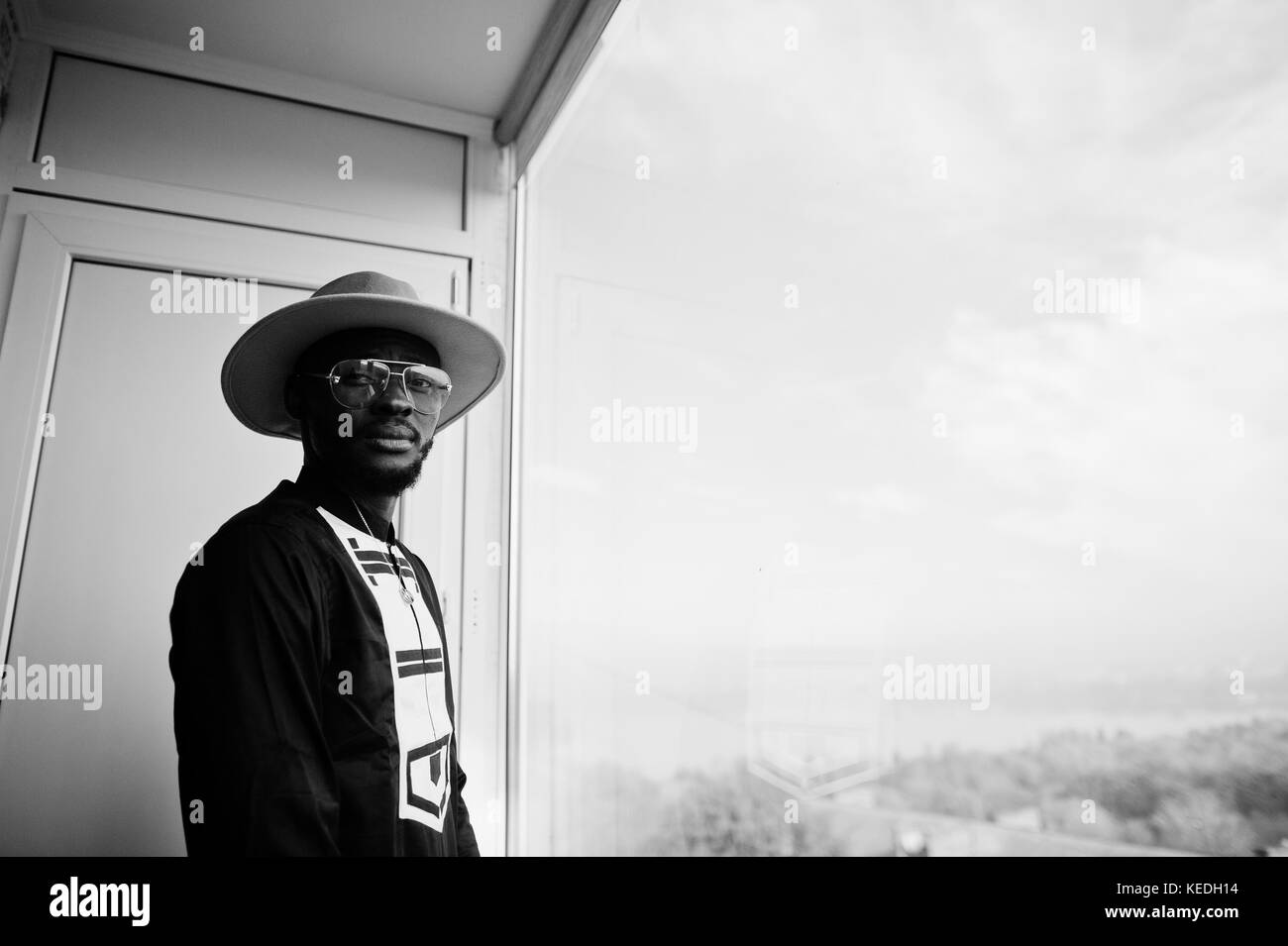 De l'Afrique riche man looking at fenêtre panoramique à son penthouse. portrait d'homme noir à hat à l'intérieur. Banque D'Images