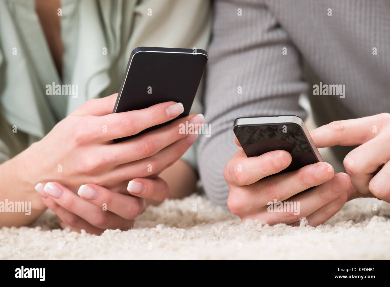 Close-up of couple holding cellphones couchée sur un tapis à la maison Banque D'Images
