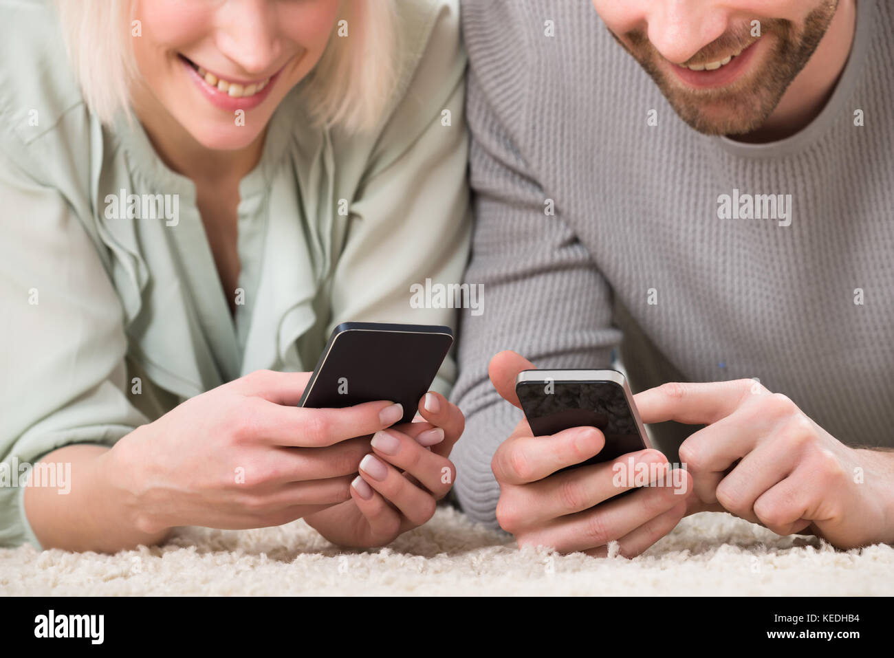 Close-up of couple holding cellphones couchée sur un tapis à la maison Banque D'Images