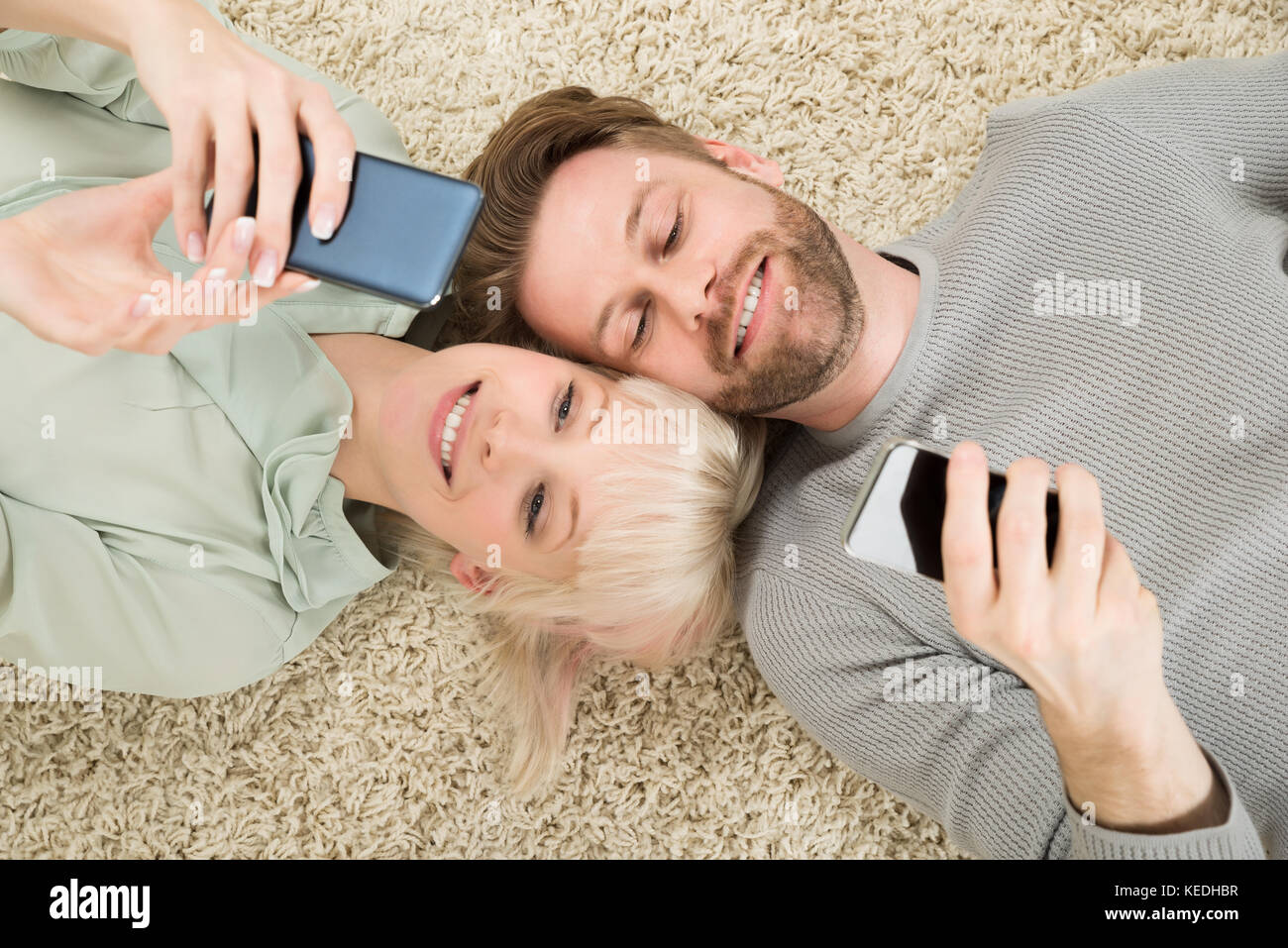 Close-up of happy couple lying on carpet l'utilisation de téléphones cellulaires Banque D'Images