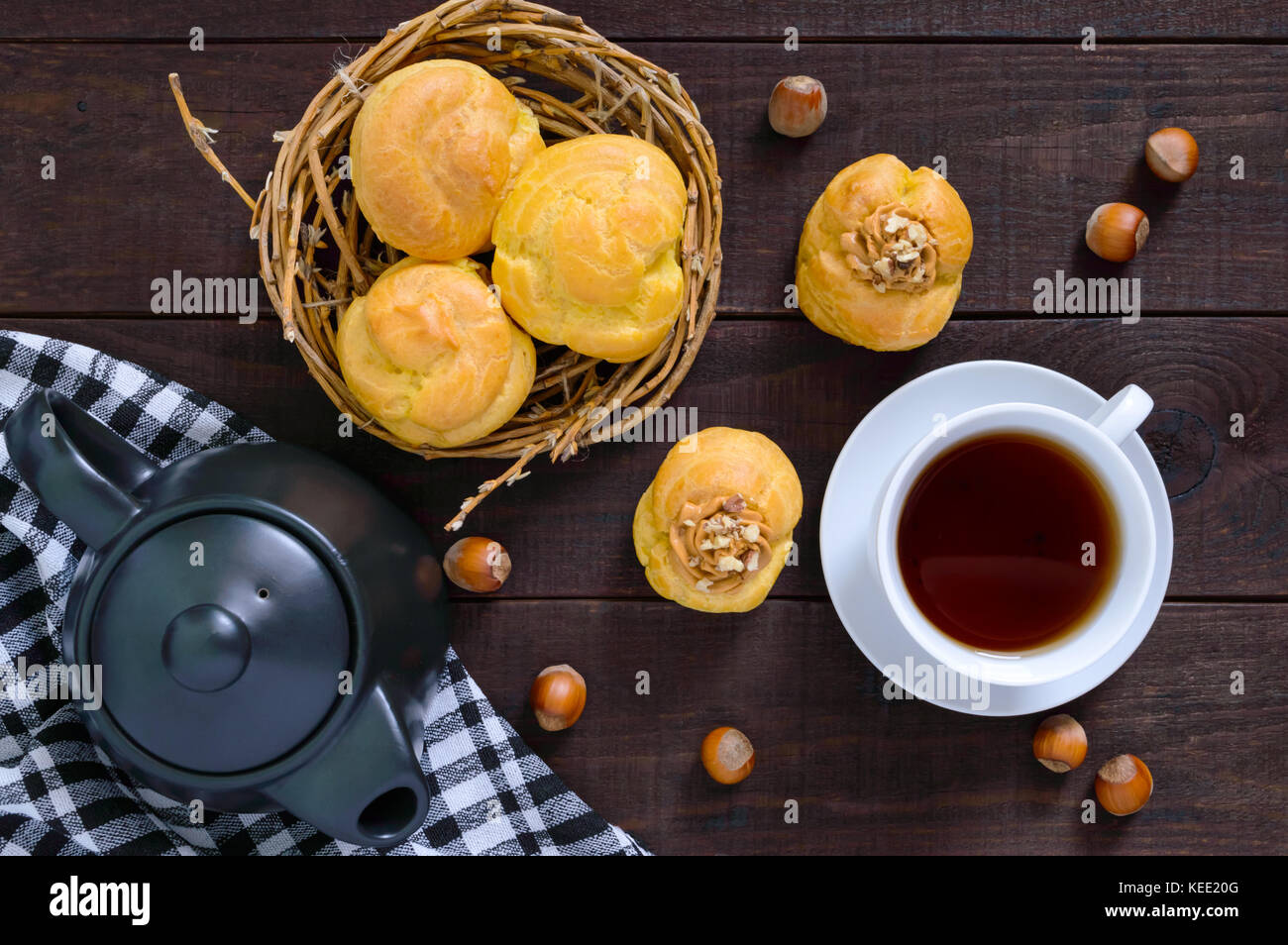 Profiteroles d'air rempli de crème caramel aux noix, tasse de thé, théière sur un fond de bois foncé. vue d'en haut. Banque D'Images