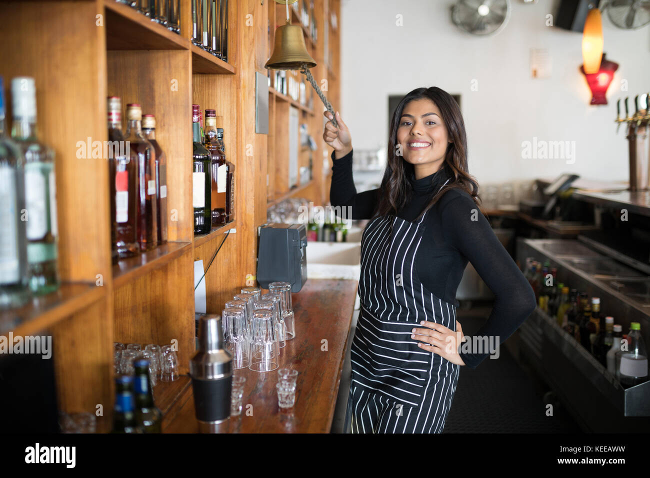 Portrait of smiling waitress cloche qui sonne au comptoir de bar Banque D'Images