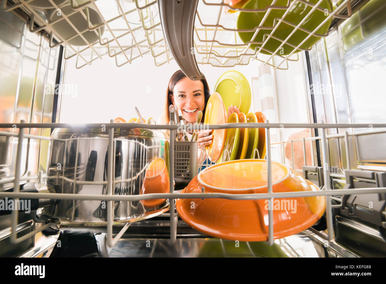 Jeune femme heureuse d'arranger des assiettes au lave-vaisselle Banque D'Images