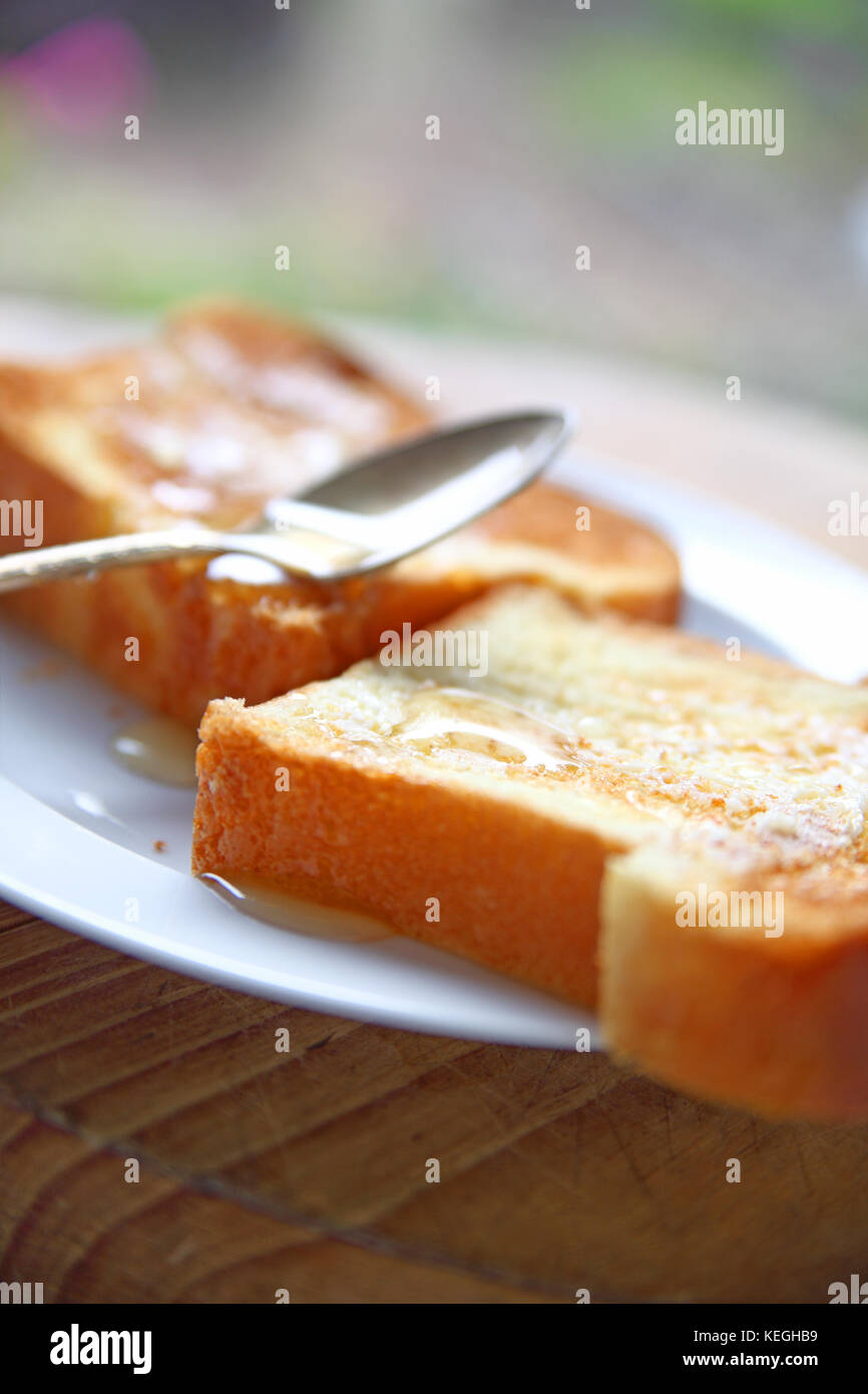 Deux tranches de brioche façon pain perdu avec propagation du beurre et du miel non filtré avec cuillère Banque D'Images