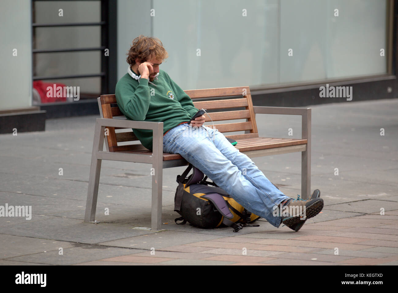 Seul homme à l'aide de la main tendue du smartphone sur le front sac à dos, assis sur un banc sur la rue Buchanan glasgow le style mile Banque D'Images